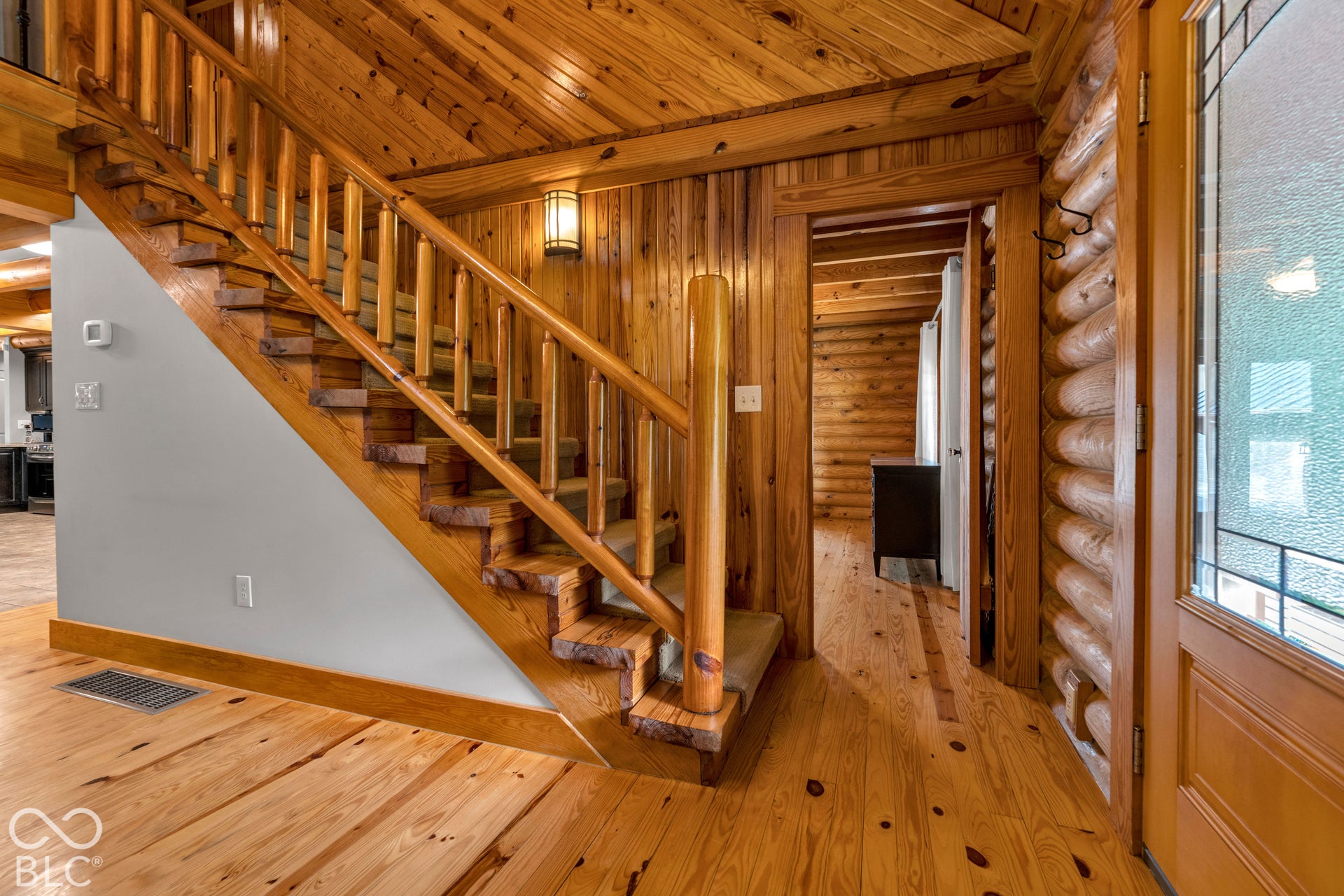 Wood-finish flooring, wood plank walls, exposed wood ceiling, wood staircase with carpeted treads, and log-style wall details