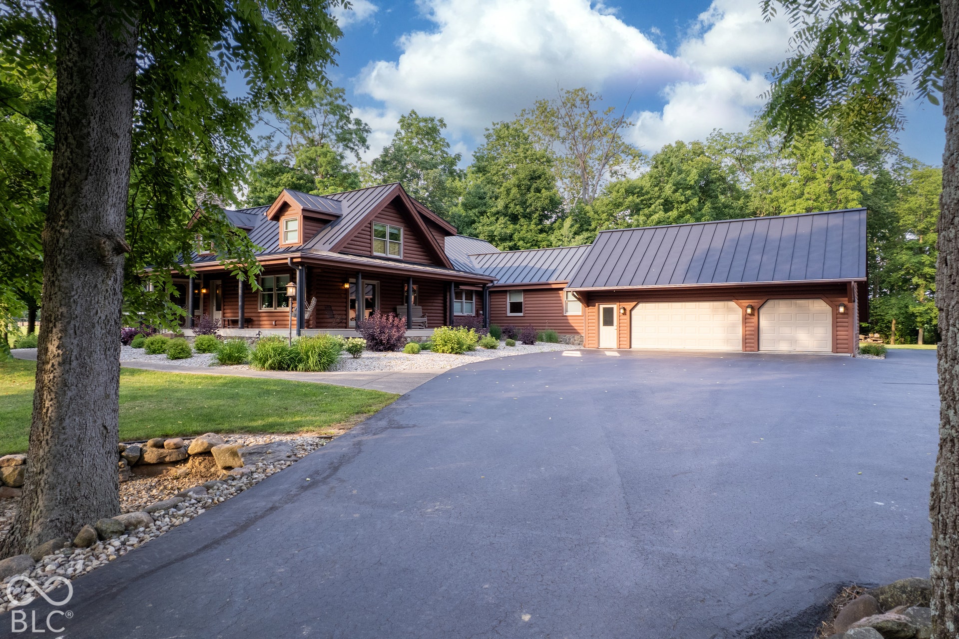 Cedar-sided residence featuring a dark metal roof, expansive paved driveway, and an attached two-car garage with overhead doors
