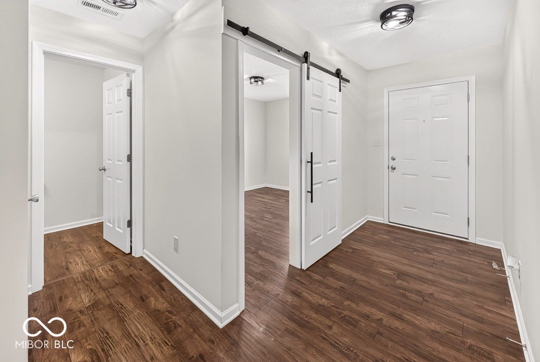 Wood-finish flooring throughout, white paneled doors, modern black track lighting, and a white front entry door