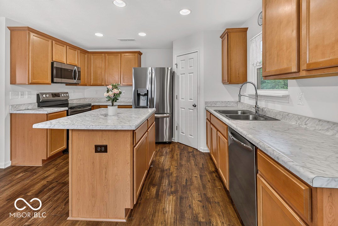 Kitchen featuring wood-finish flooring, wood cabinetry, light-toned countertops, stainless steel appliances, and a central island
