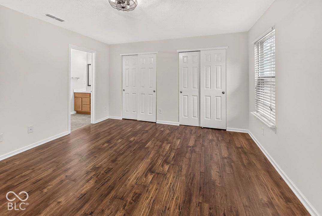 Wood-finish flooring, white walls, multiple closet doors, window with blinds, and ceiling light fixture