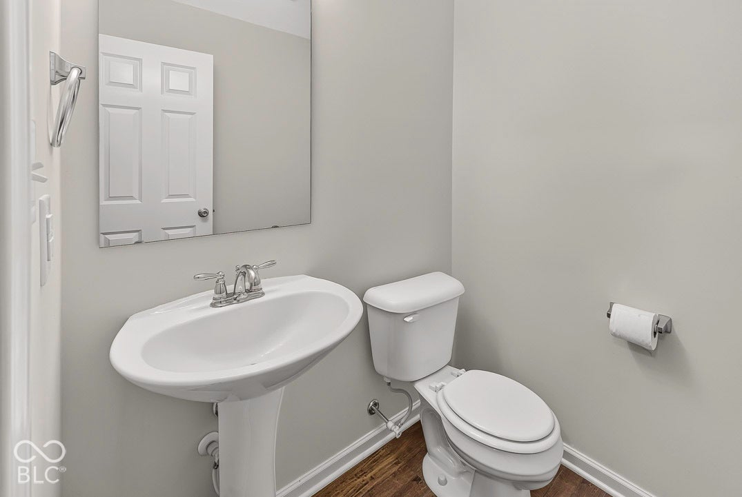 Pedestal sink with chrome faucet, toilet, wall-mounted mirror, and wood-finish flooring
