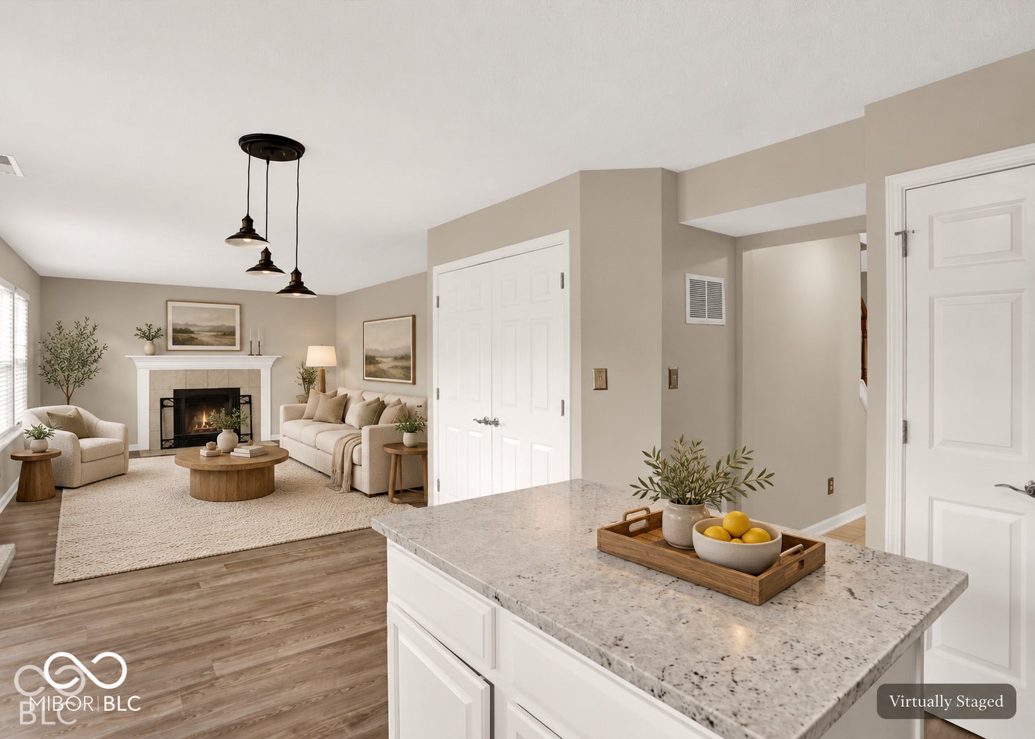 Wood-finish flooring, white kitchen cabinetry with light-toned countertops, a fireplace with a white mantel, and a multi-pendant ceiling light fixture
