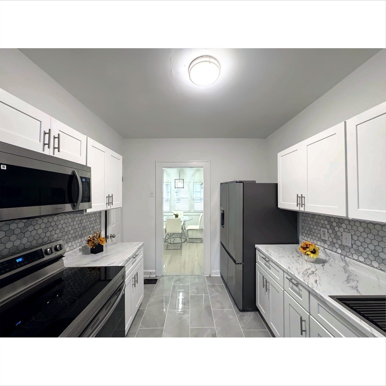 Modern kitchen featuring white shaker cabinetry, stainless steel appliances, honeycomb tile backsplash, and light-toned tile flooring