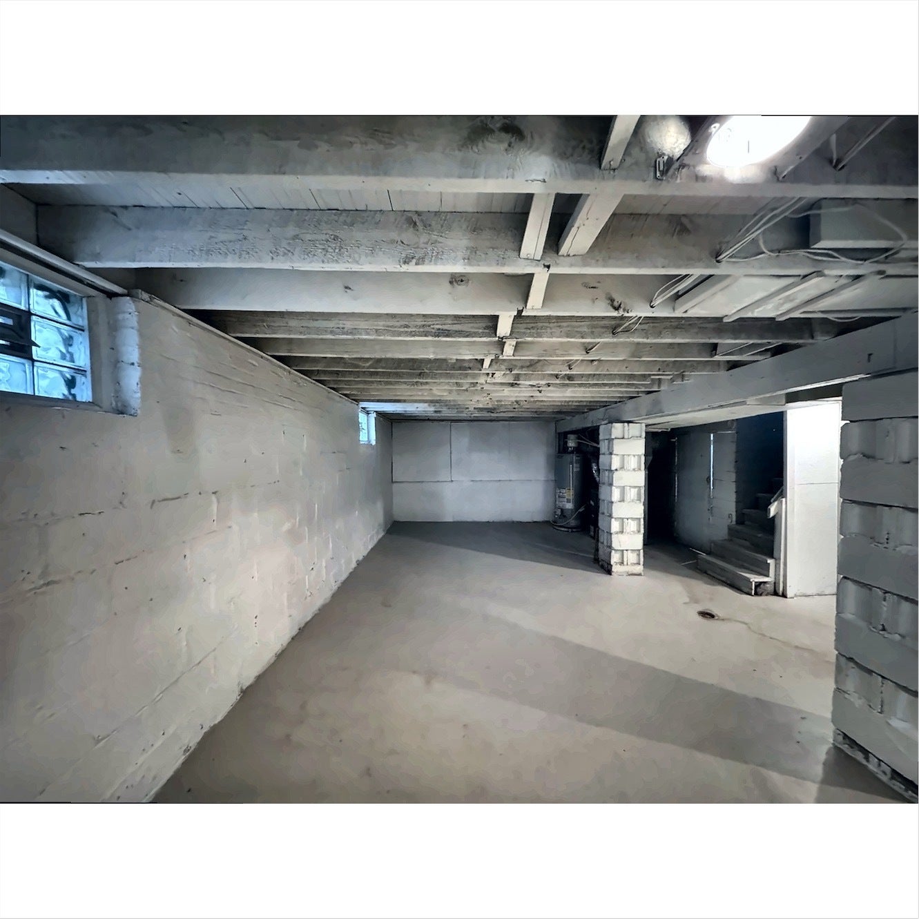 Finished concrete flooring, exposed ceiling joists, painted block walls, glass block windows, and structural support columns