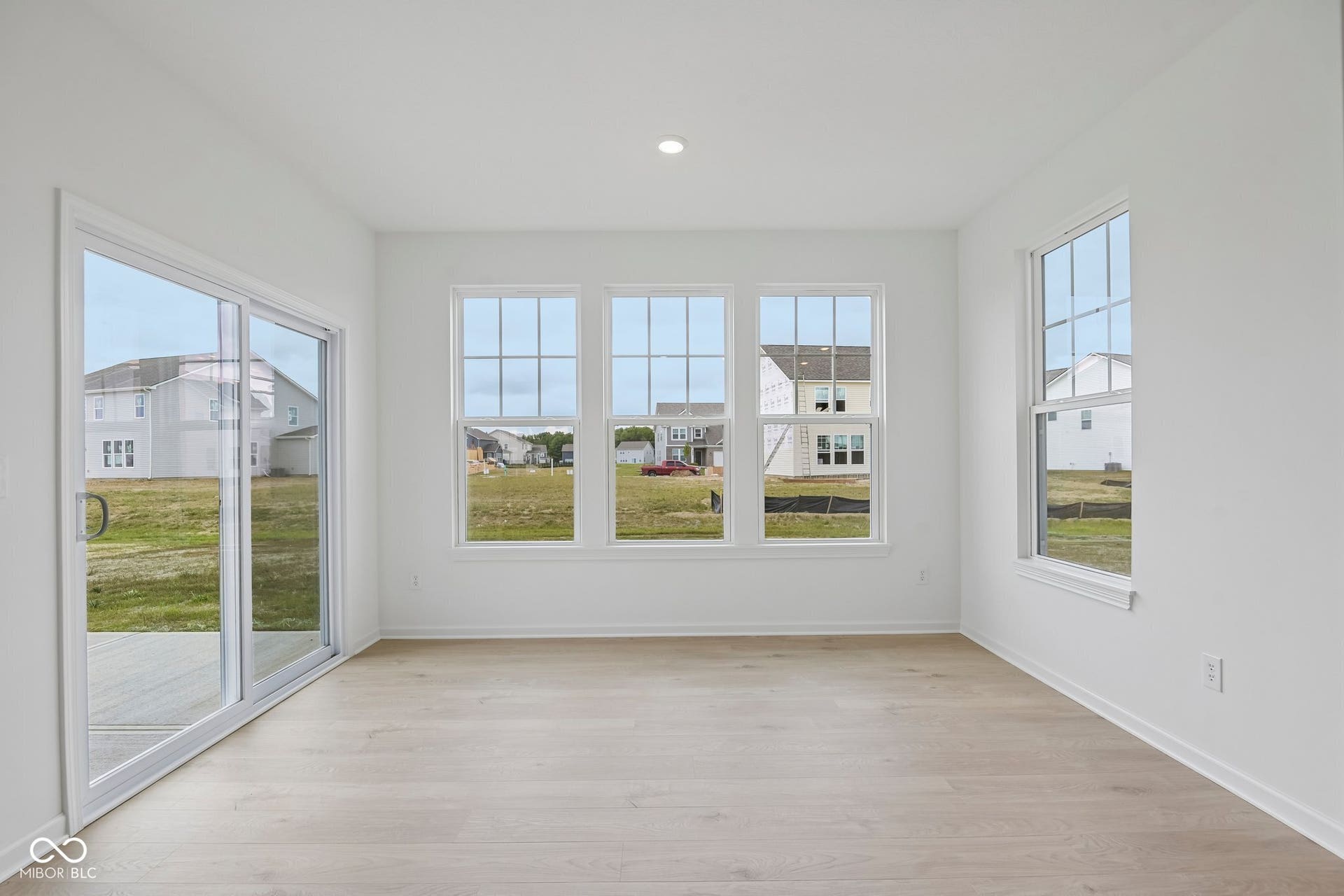 Spacious interior featuring wood-finish flooring, white walls, multiple windows, and a sliding glass door