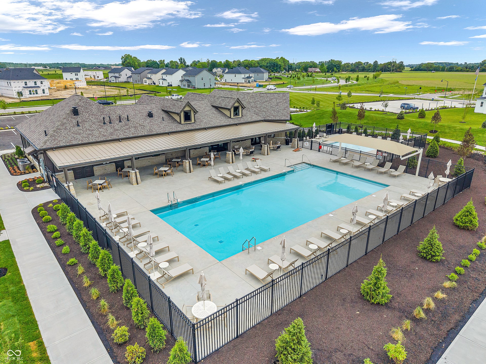 Resort-style saltwater pool with expansive concrete decking, black metal perimeter fencing, and a modern poolhouse featuring covered lounge areas