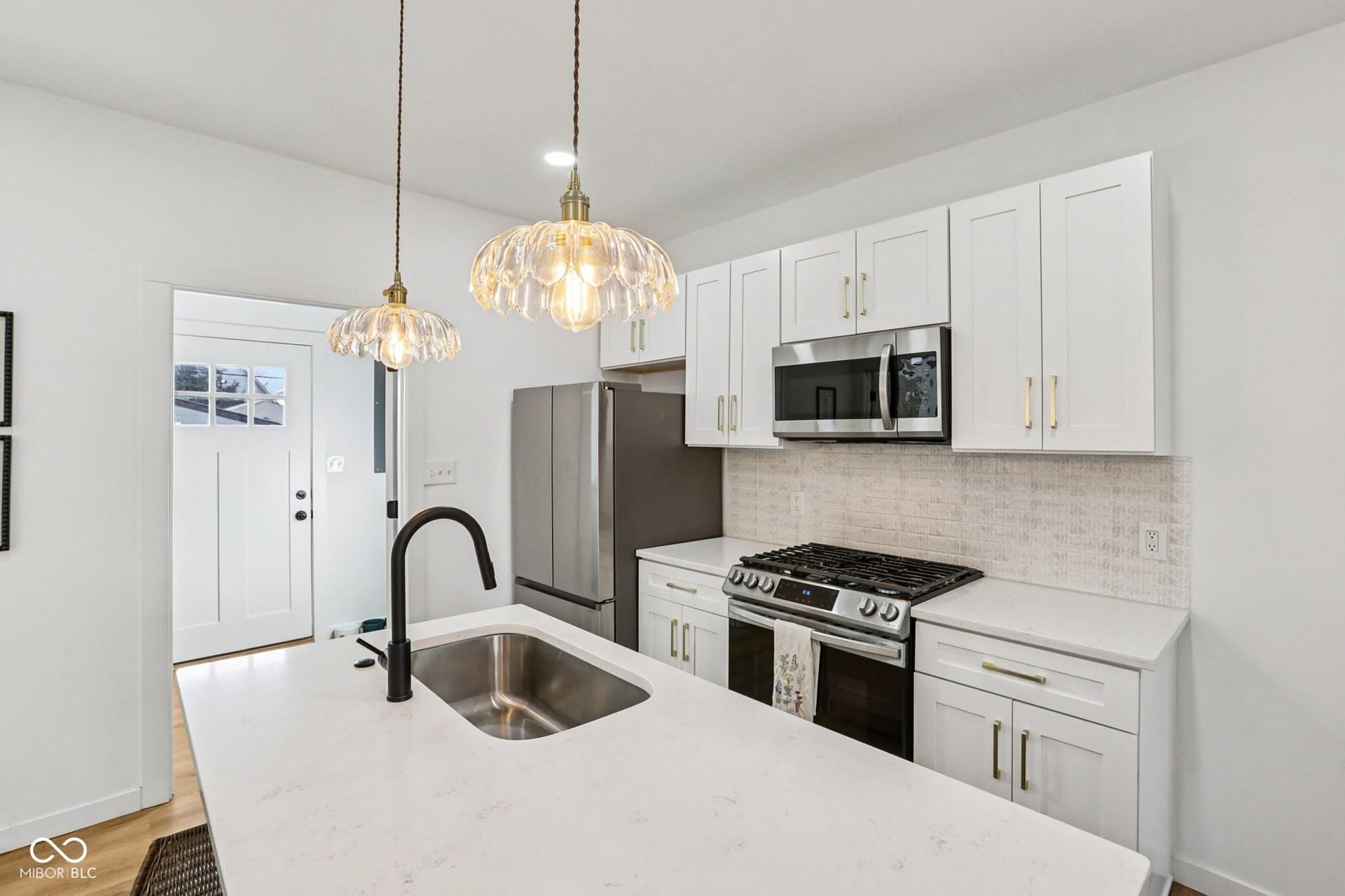 Kitchen featuring white shaker-style cabinetry, stainless steel appliances, a gas range with an overhead microwave, and a textured subway tile backsplash