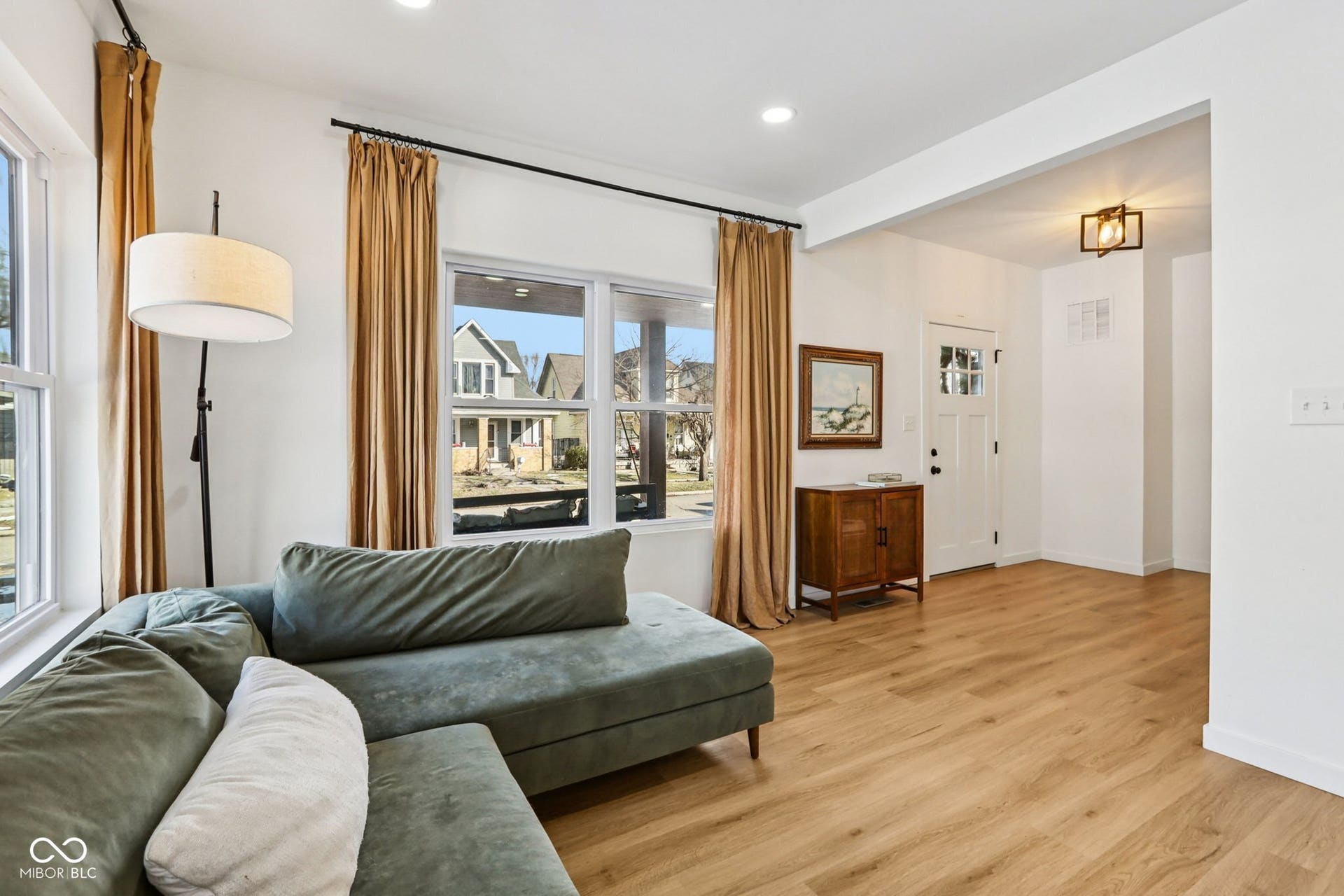 Bright living area featuring wood-finish flooring, white walls, multiple windows, and a craftsman-style entry door