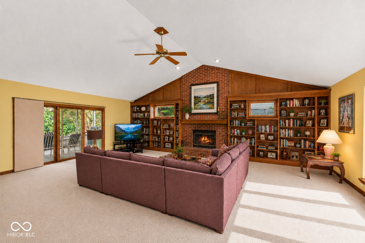 Vaulted ceiling with a ceiling fan, brick fireplace, built-in wooden shelving, and access to screened-in patio