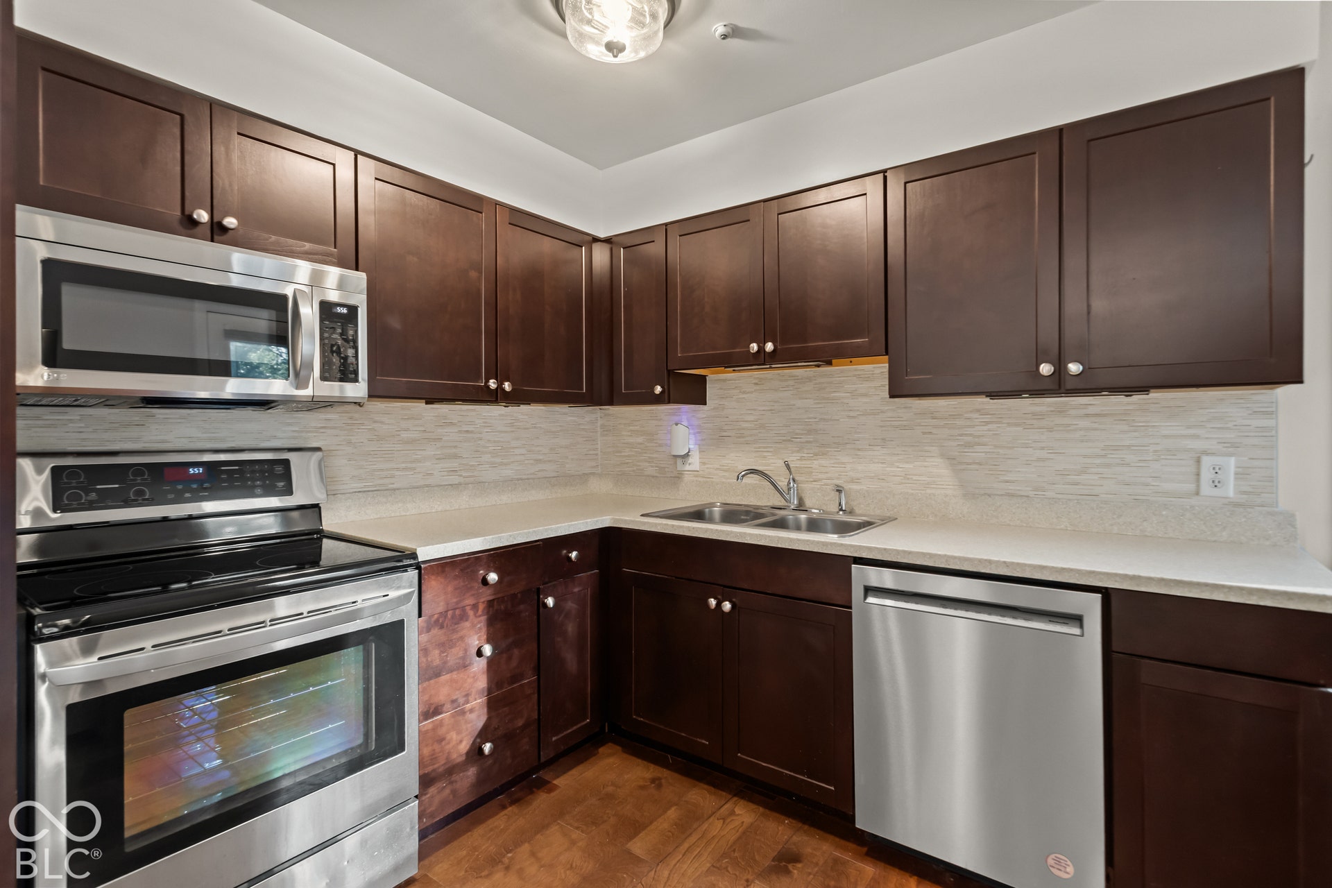 Dark wood-finish cabinetry, stainless steel appliances, light-toned countertops, and wood-finish flooring