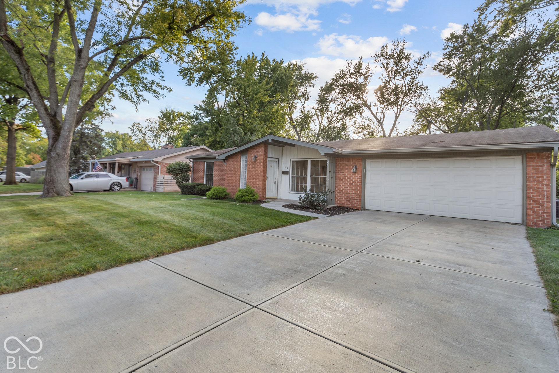 Brick and siding exterior, two-car garage, concrete driveway, front yard with mature trees, and established landscaping