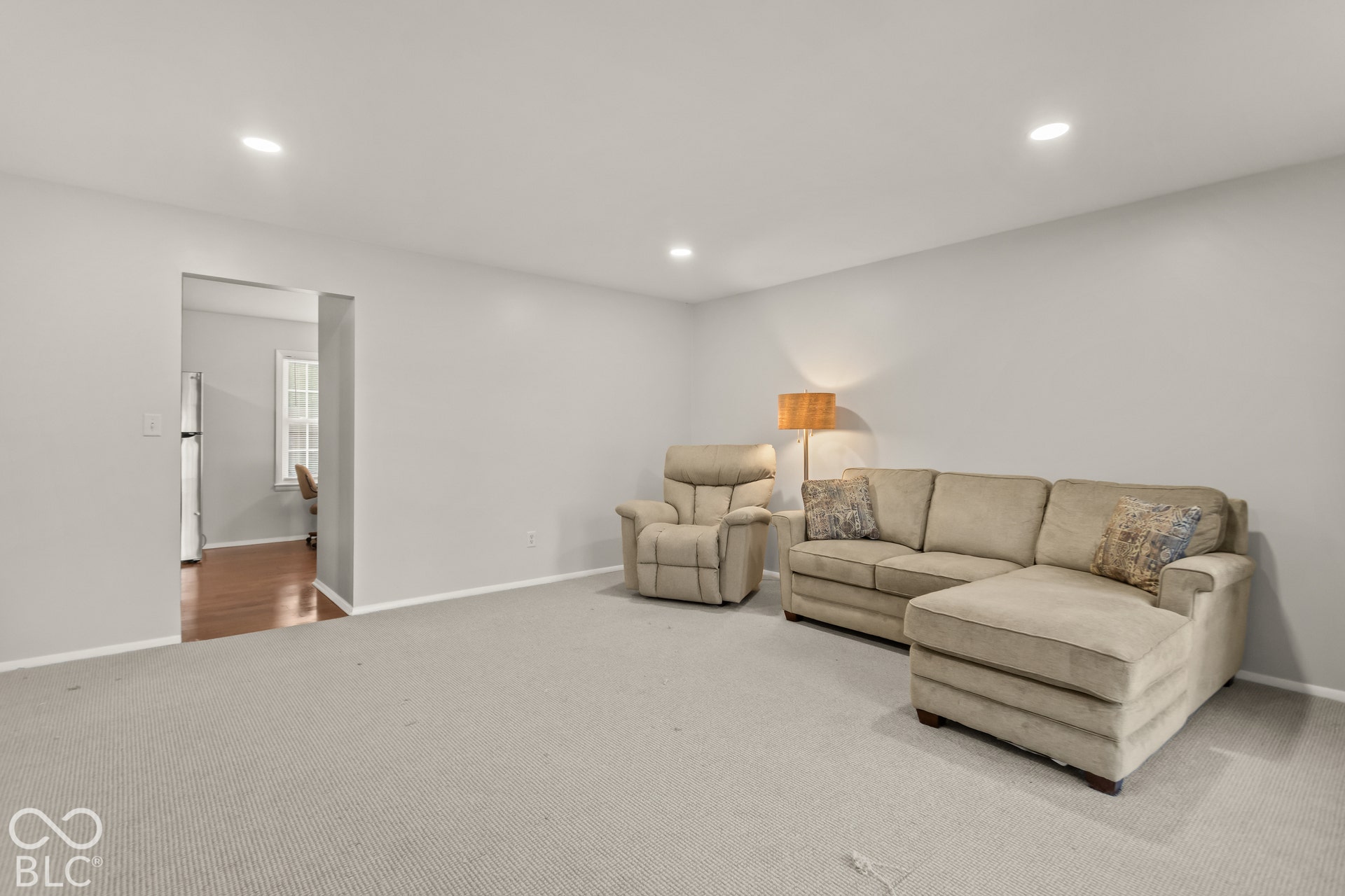 Recessed ceiling lighting illuminates a spacious room featuring light-toned carpeting and neutral wall finishes