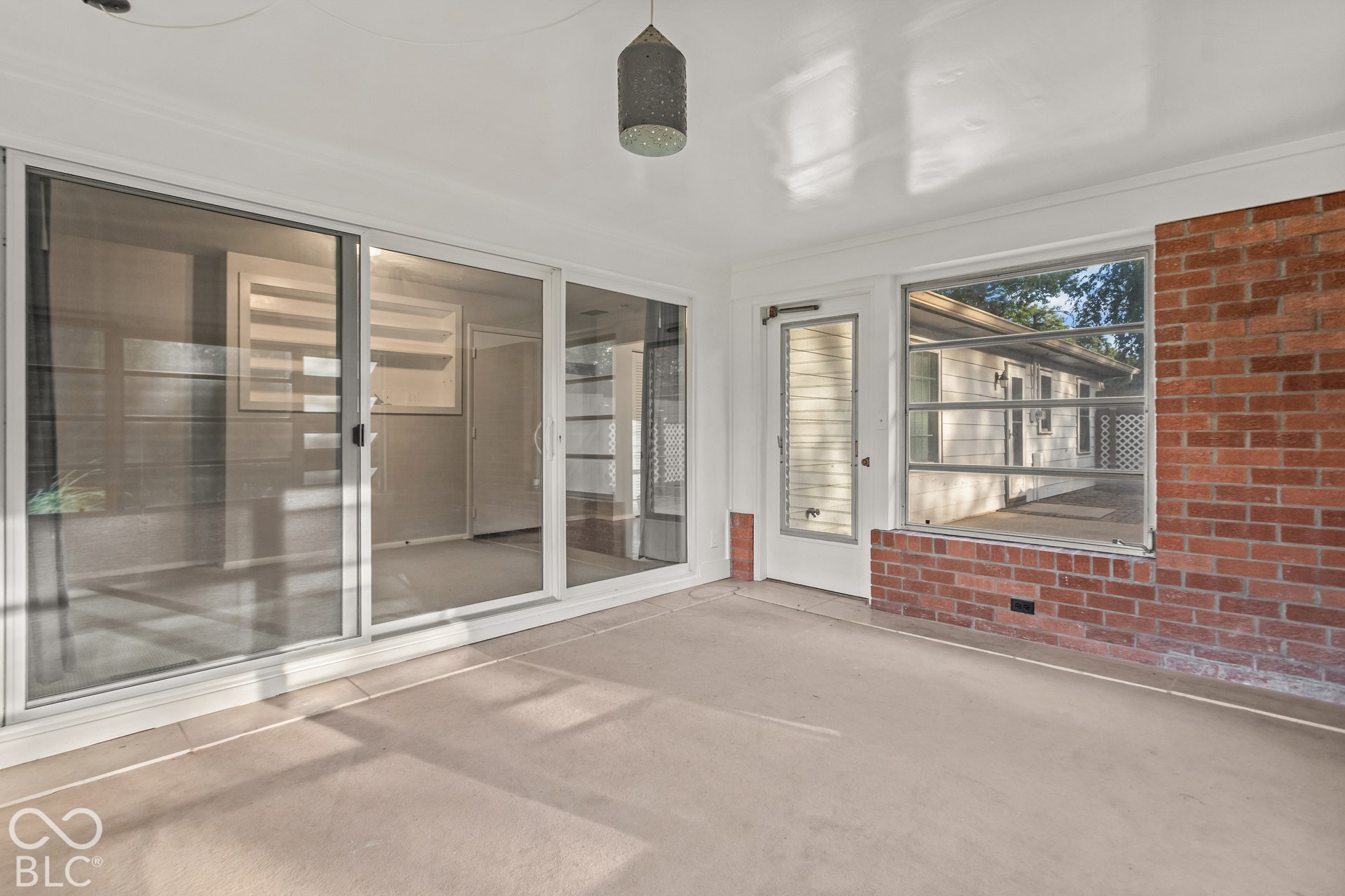 Enclosed sunroom featuring expansive sliding glass doors, brick half-walls, and a durable concrete floor