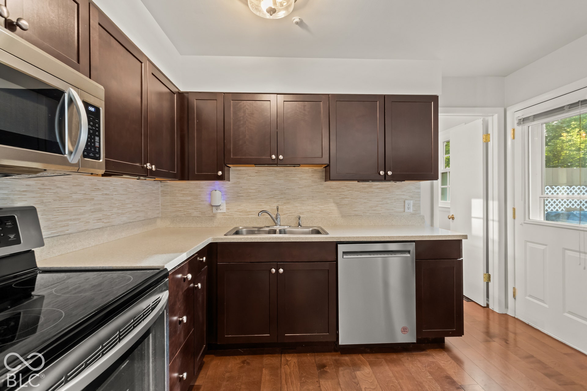 Kitchen featuring dark wood-finish cabinetry, stainless steel appliances, a light-toned countertop, and wood-finish flooring