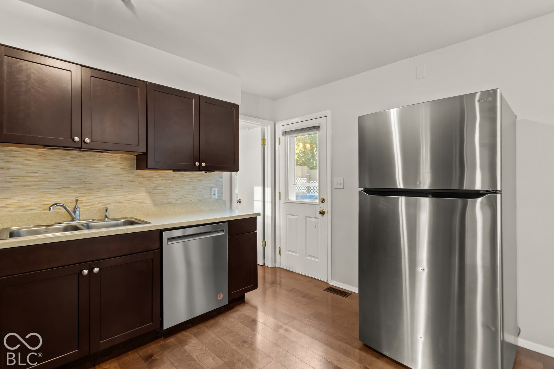 Kitchen featuring dark wood-finish cabinetry, stainless steel dishwasher, stainless steel refrigerator, and wood-finish flooring