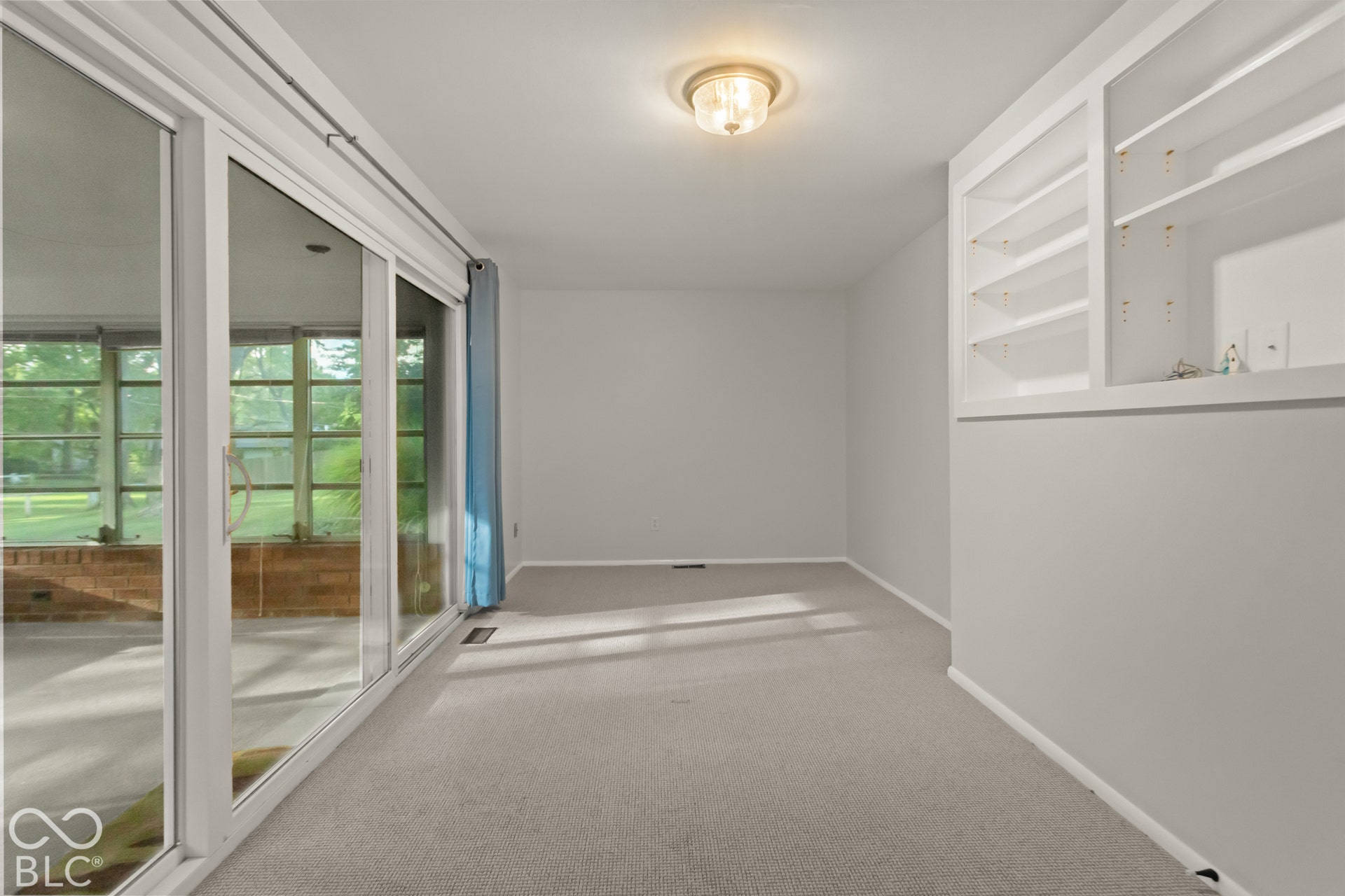 Built-in shelving, flush-mount ceiling light, light-toned carpeting, and a sliding glass door