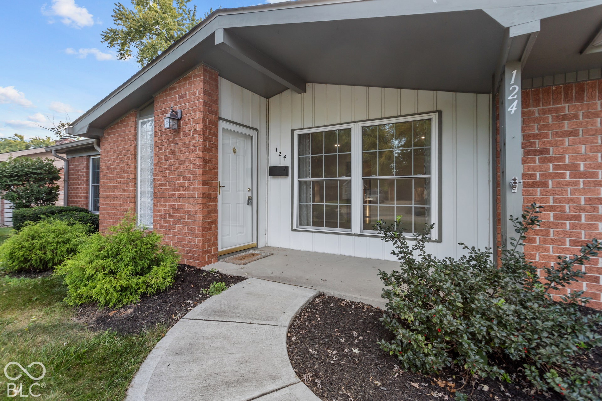 Brick and siding exterior with covered entry, multiple windows, and a curved concrete walkway