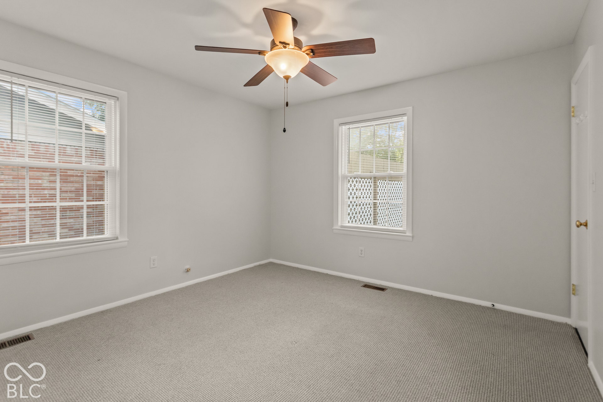 Carpeted room featuring two windows with white frames, a ceiling fan with light fixture, and light gray walls