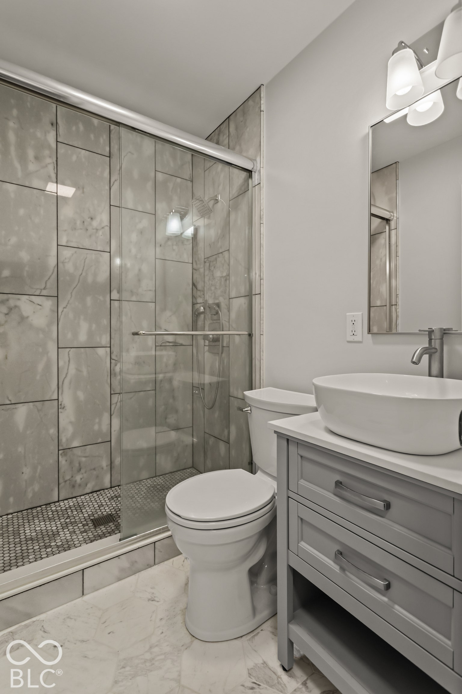 Glass-enclosed shower with large format tile surround and mosaic floor