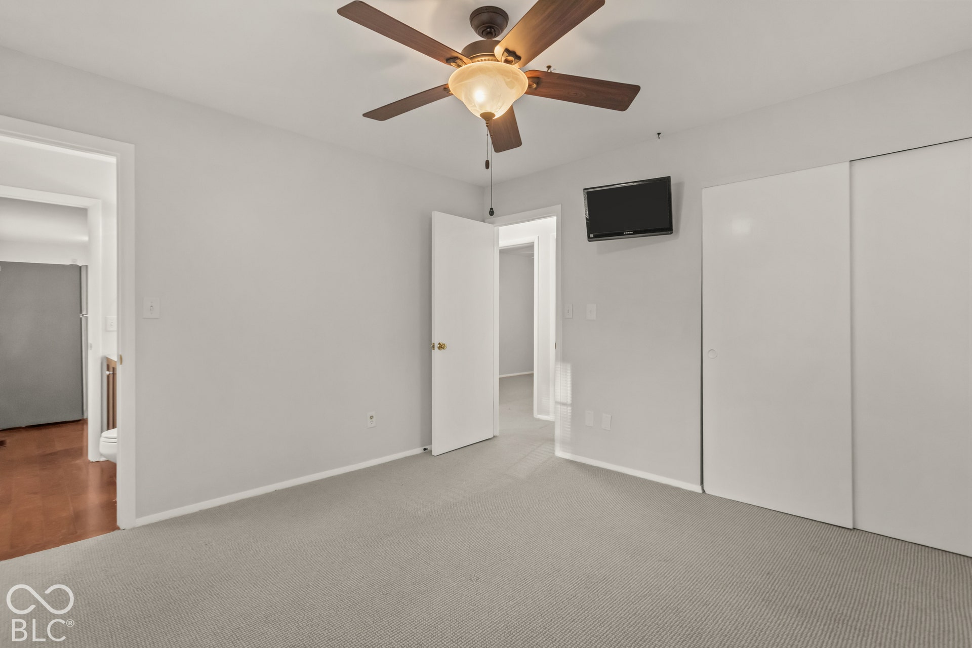 Neutral-toned carpet flooring with a ceiling fan light fixture and dual sliding closet doors