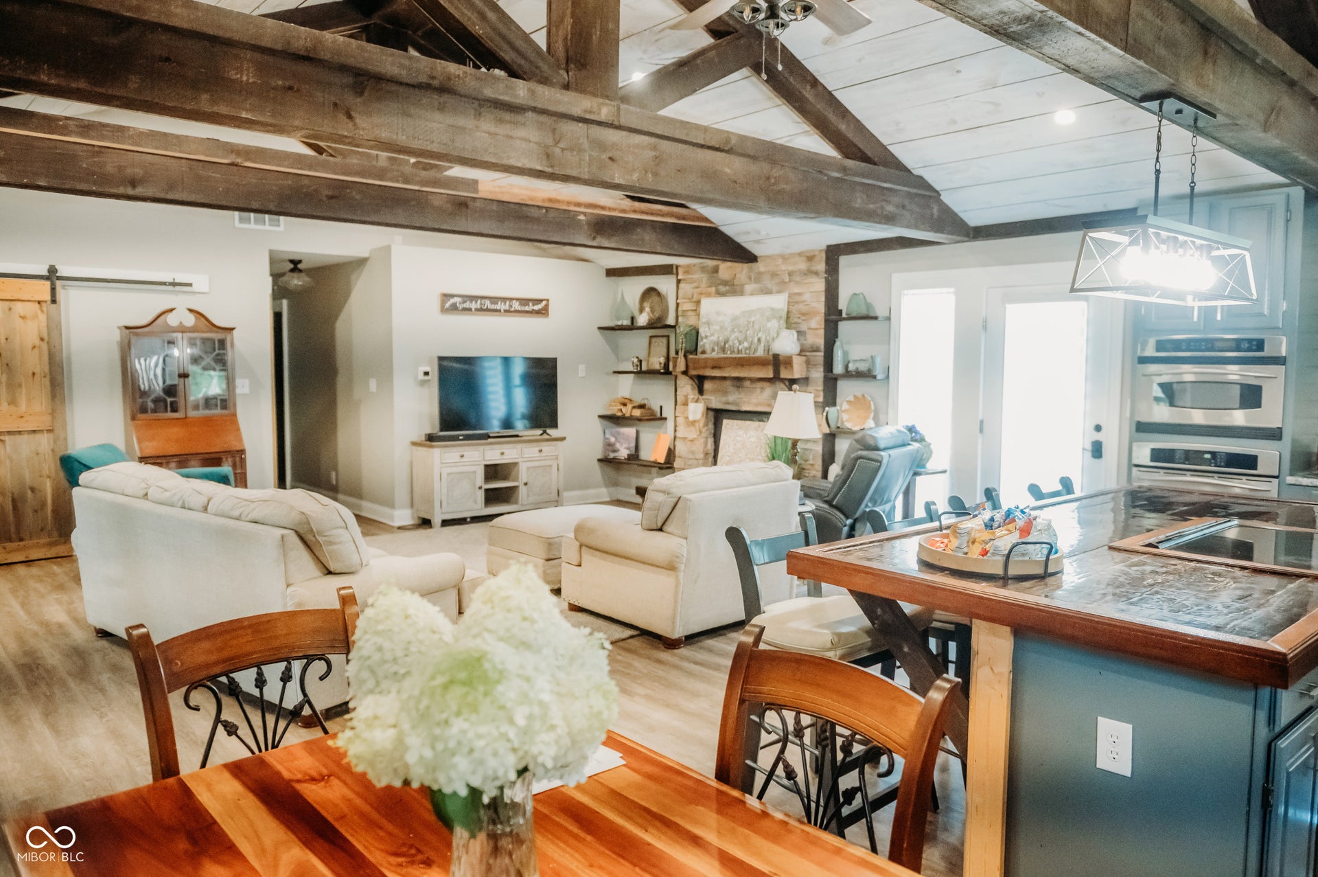 Vaulted ceiling with exposed wood beams, wood-finish flooring, and a stone fireplace with a wood mantel