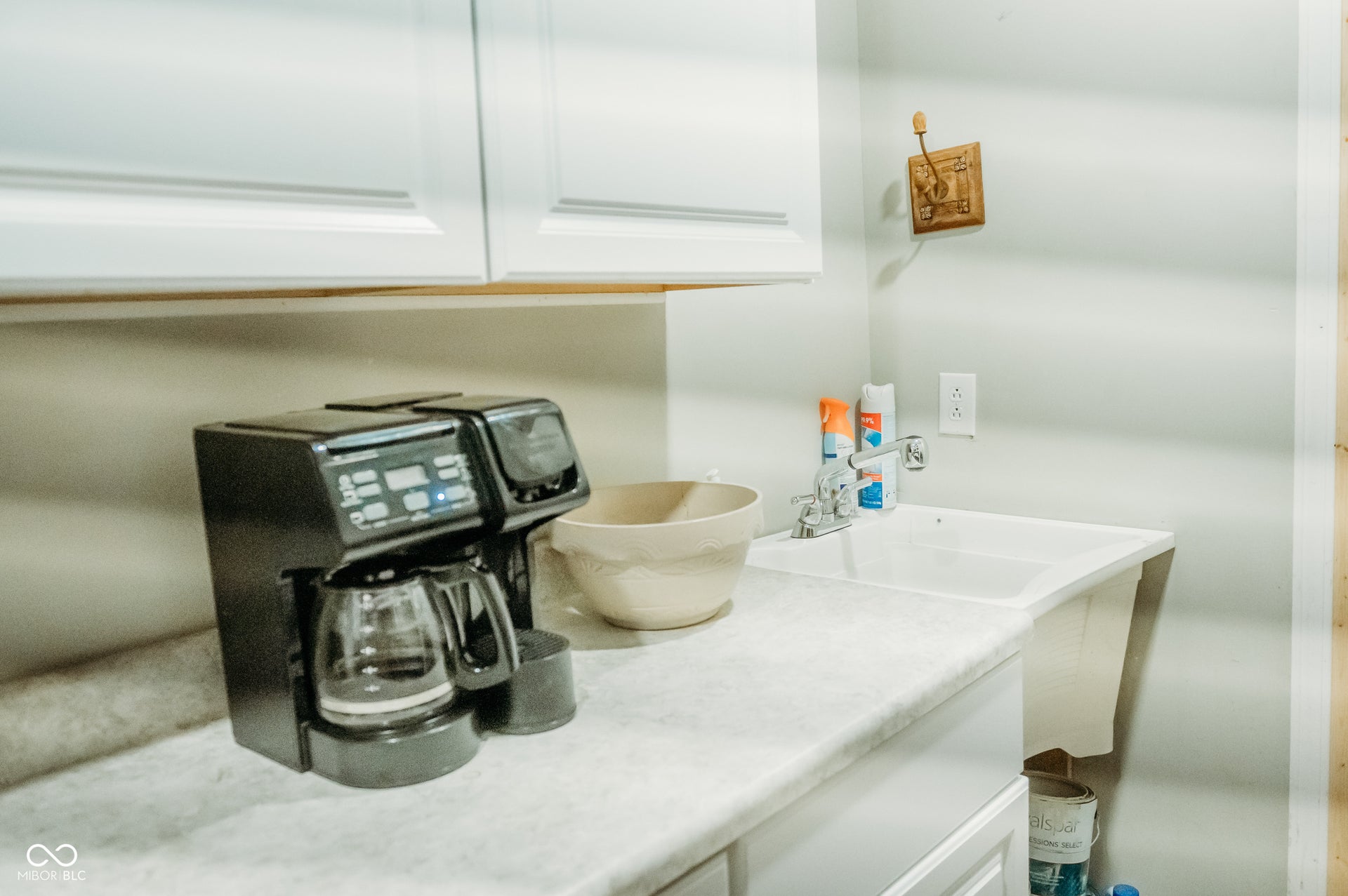 White shaker-style upper cabinetry over a light-colored countertop, featuring a built-in utility sink with a chrome faucet