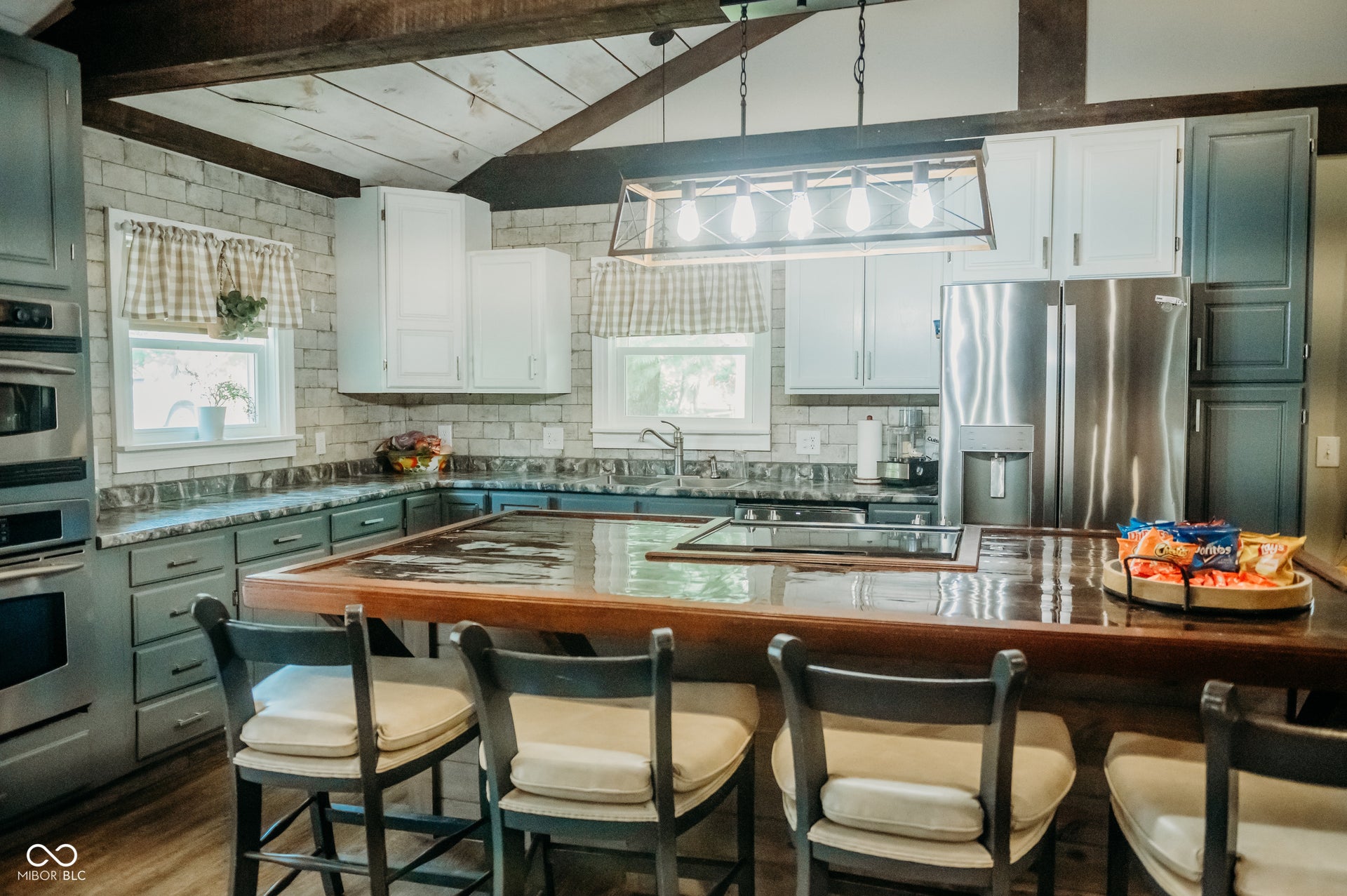 Kitchen featuring a large wood-finish island with cooktop, painted cabinetry, brick-patterned backsplash, and stainless steel appliances including a built-in oven and microwave