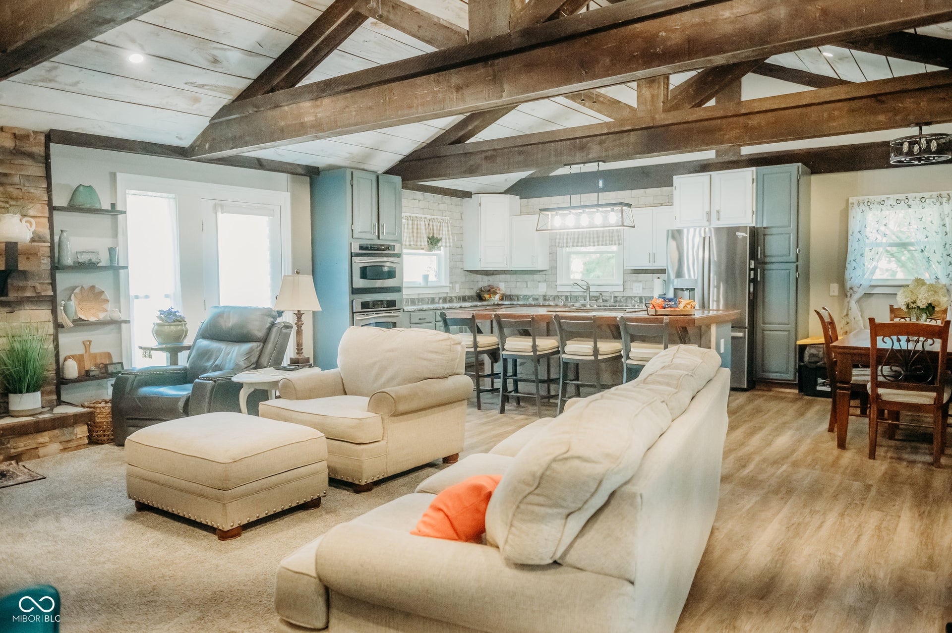 Spacious great room featuring vaulted ceilings with exposed wood beams, a stone-clad fireplace, and integrated shelving