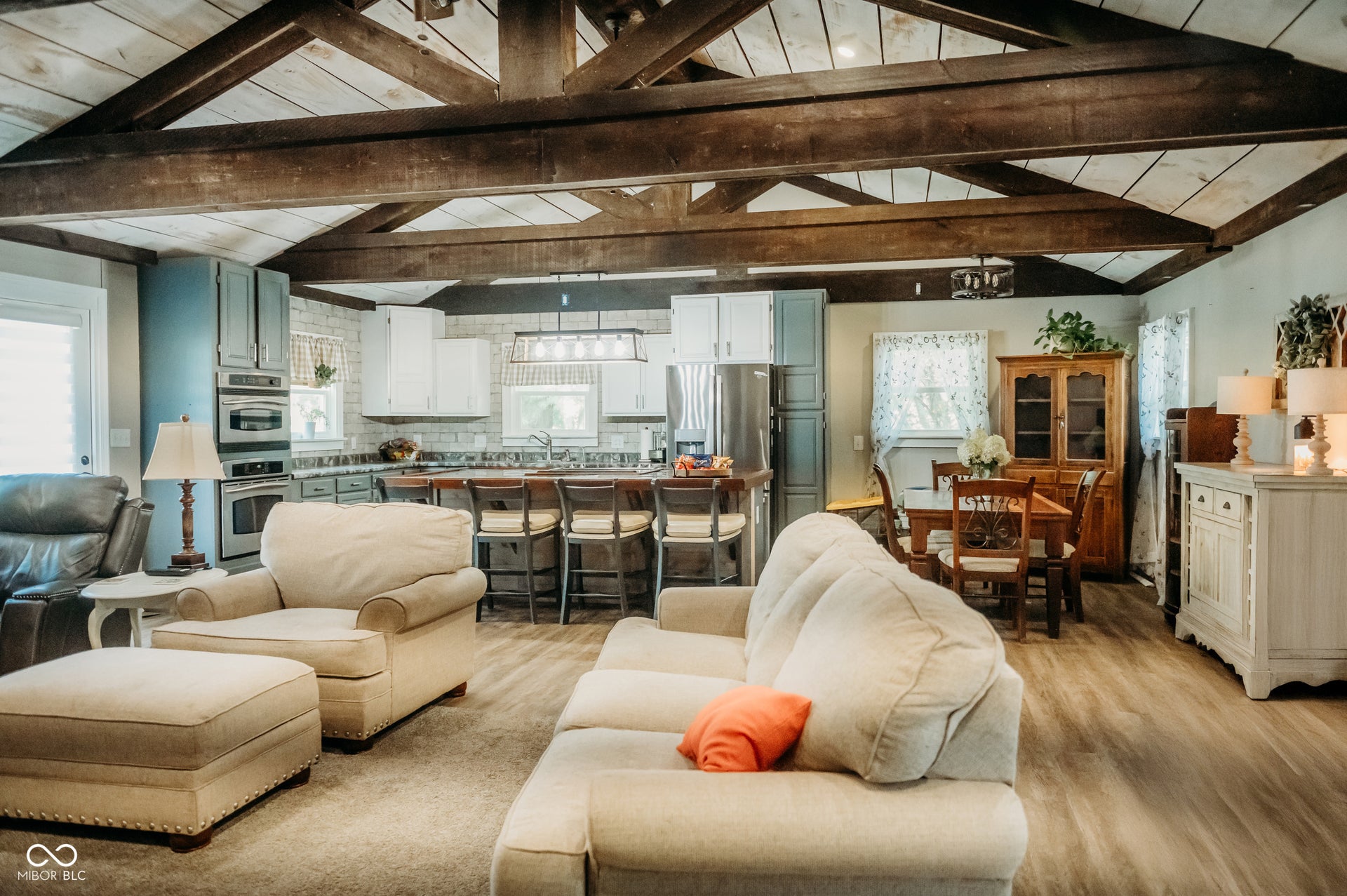 Open concept living area featuring exposed wood beams, vaulted ceilings with wood paneling, wood-finish flooring, a kitchen island with seating, and stainless steel appliances