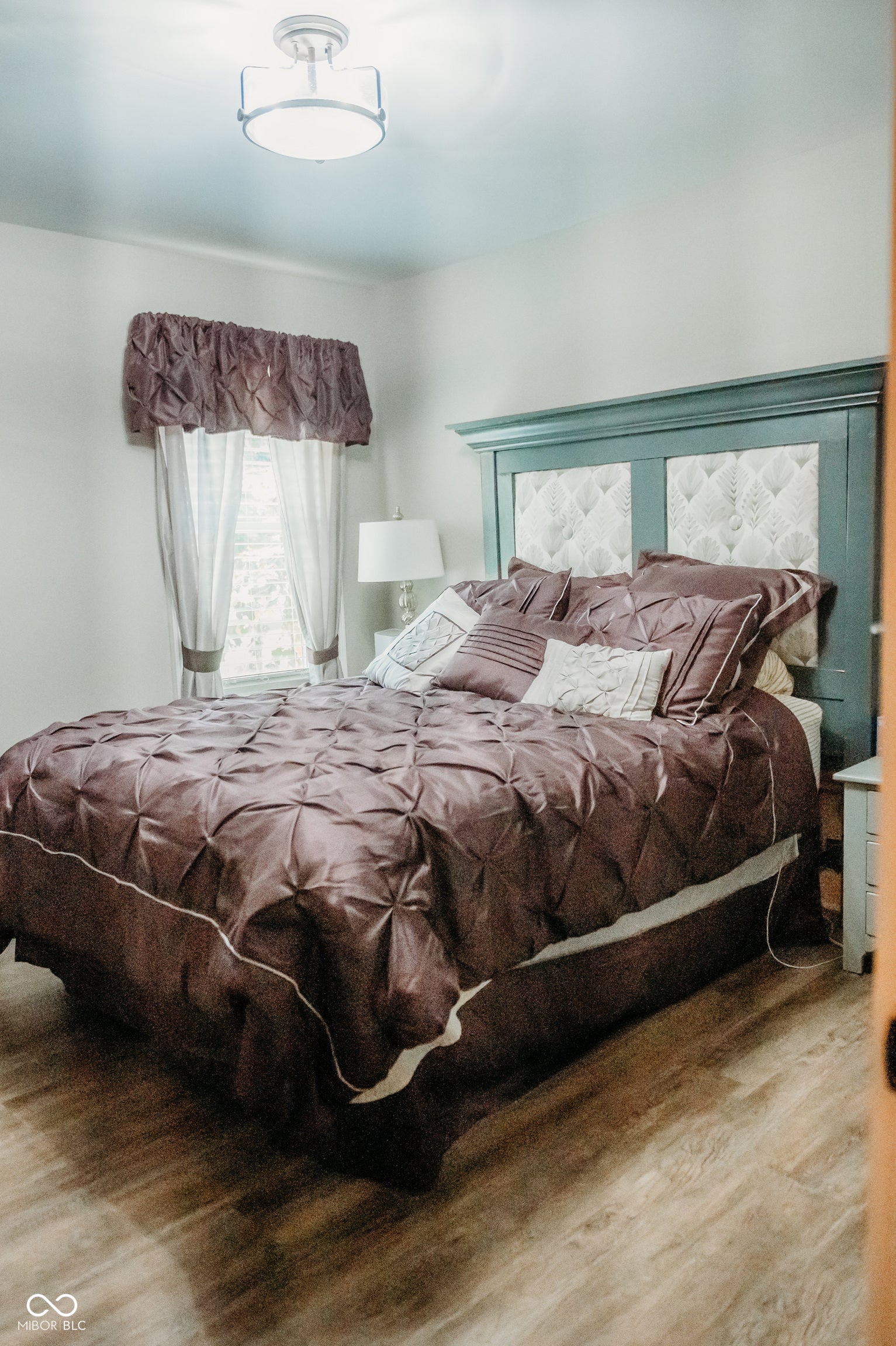 Bedroom featuring wood-finish flooring, a semi-flush mount ceiling light fixture, and a window with valance and curtains