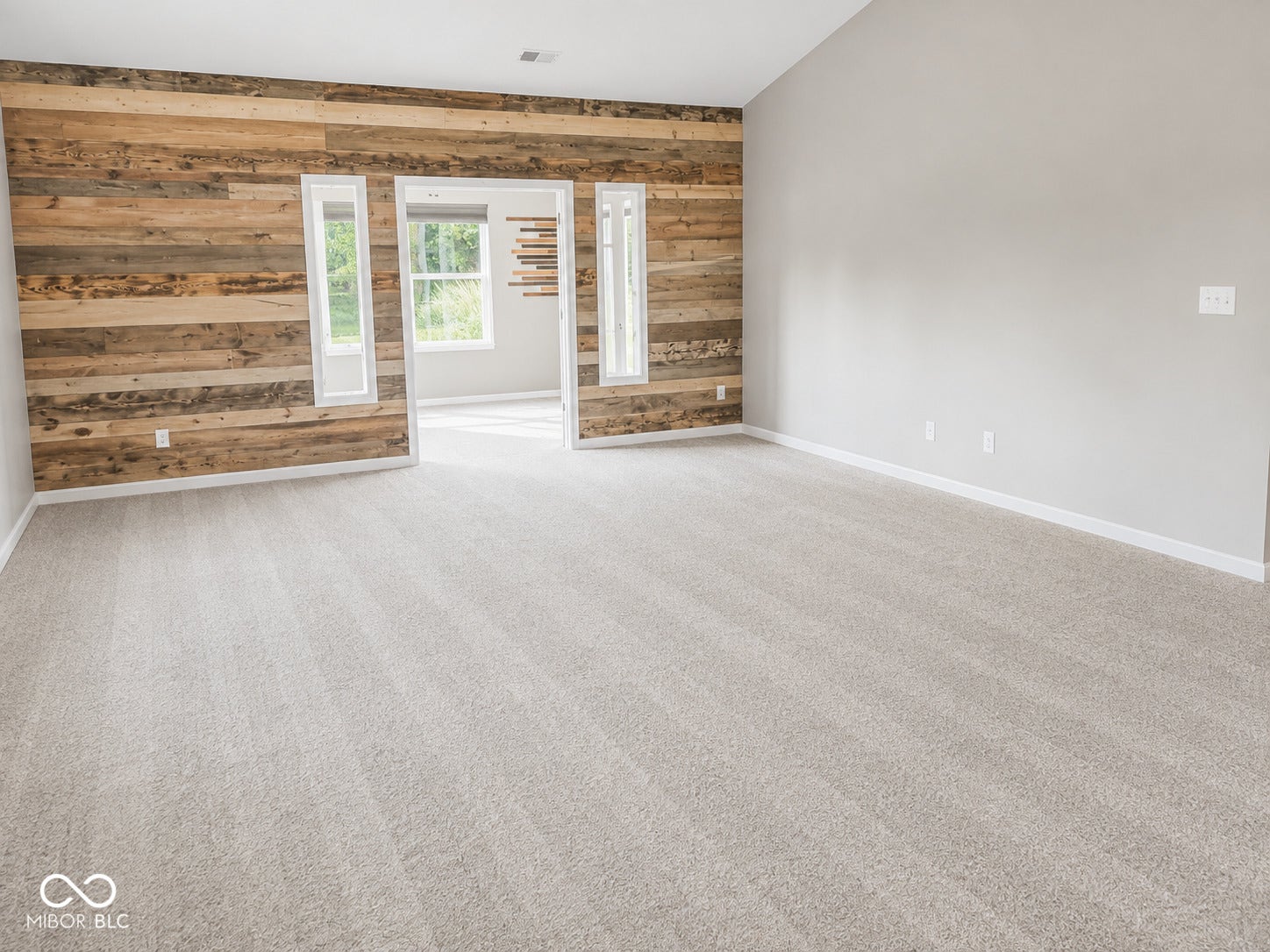 Spacious room featuring a wood-panel accent wall, neutral carpeting, and white trim