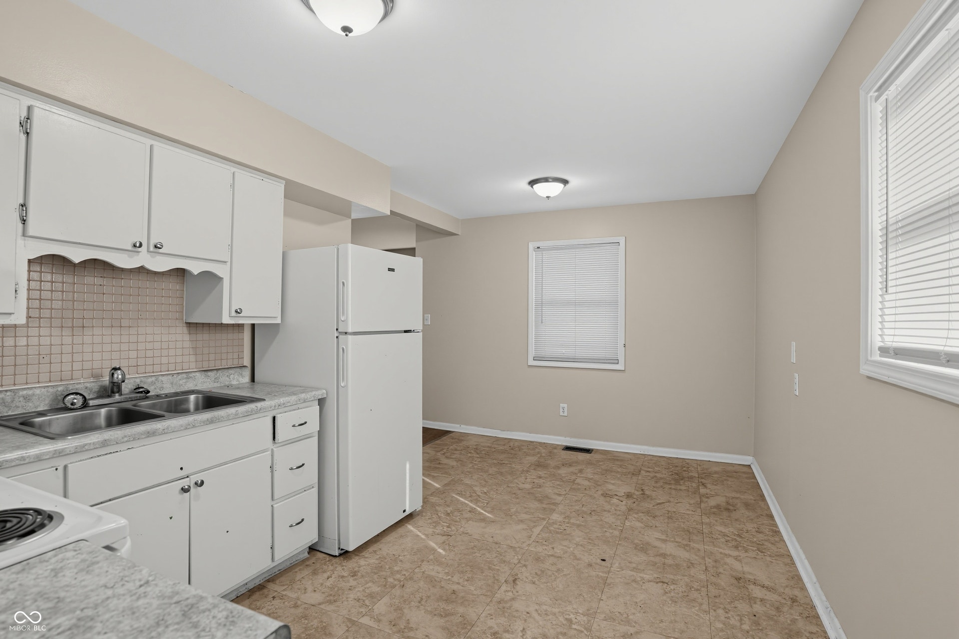Kitchen area featuring white cabinetry, a double basin sink, and a white refrigerator