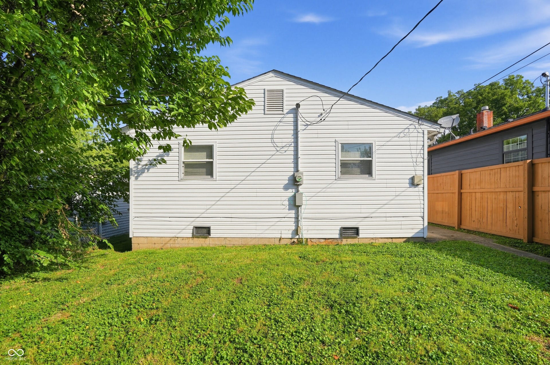 Expansive grassy yard area with a wooden privacy fence and a white siding exterior