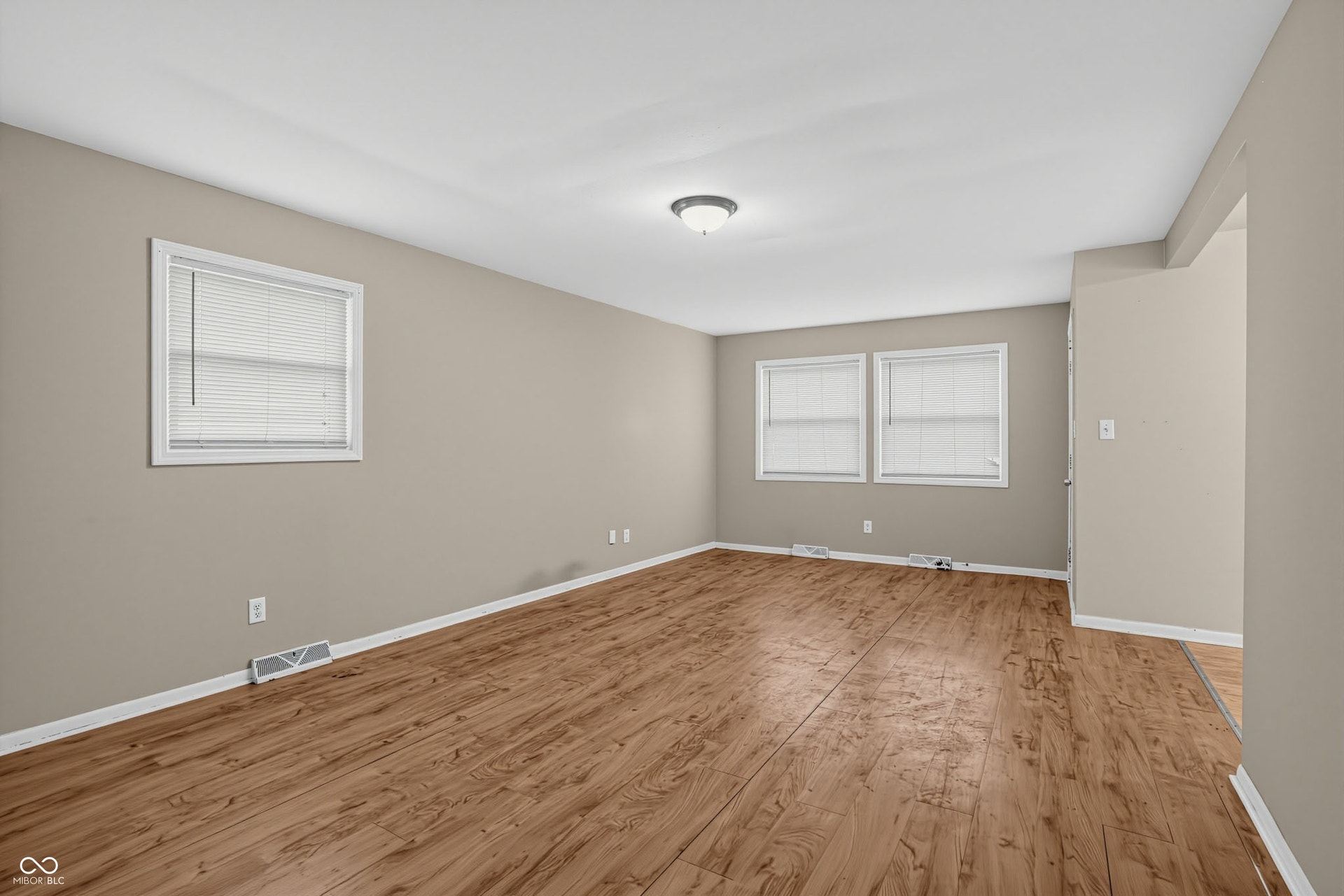 Spacious room featuring neutral wall tones, wood-finish flooring, multiple windows with blinds, and white trim throughout