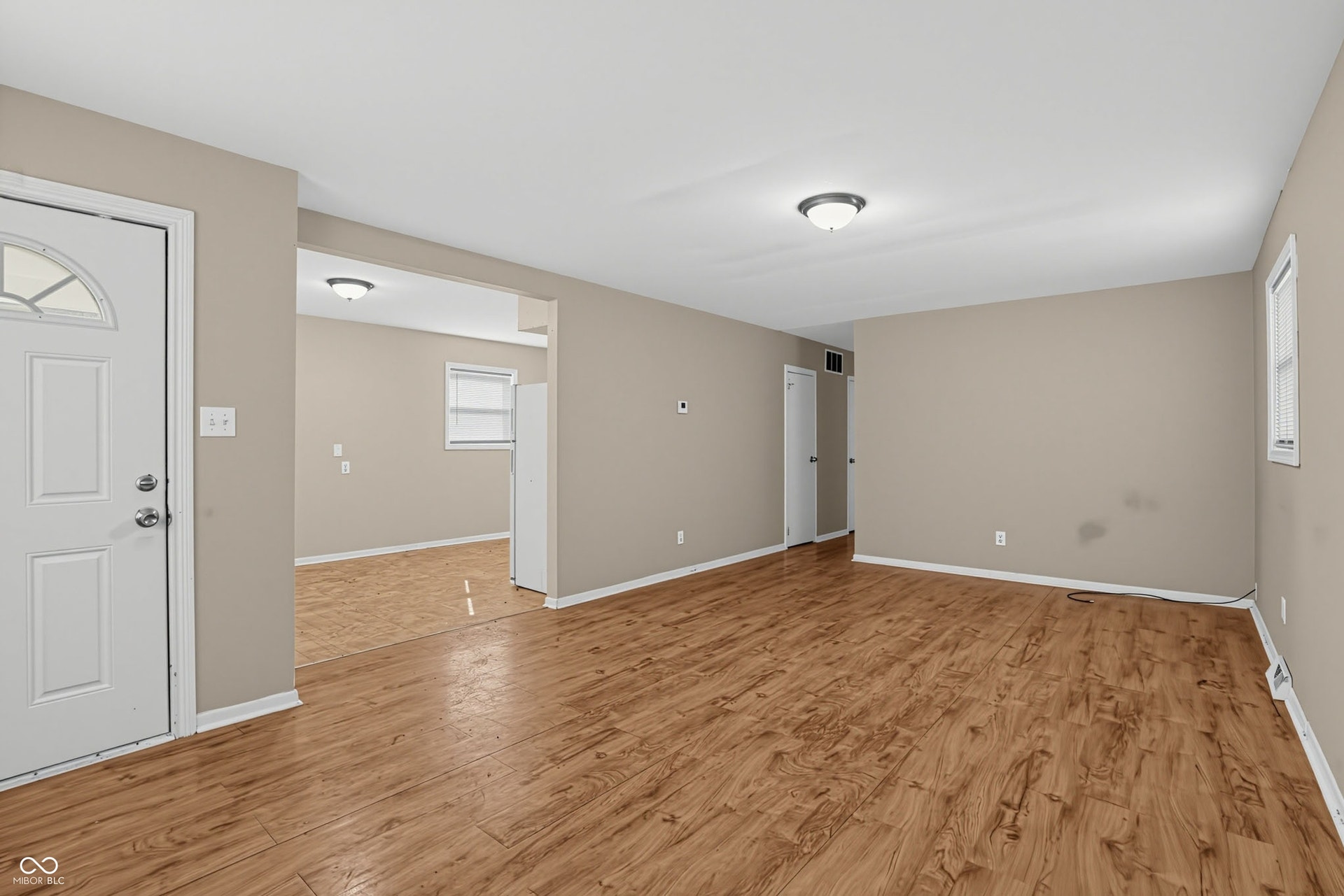 Wood-finish flooring, neutral wall tones, white interior door with arched glass insert, ceiling-mounted light fixtures, and white trim