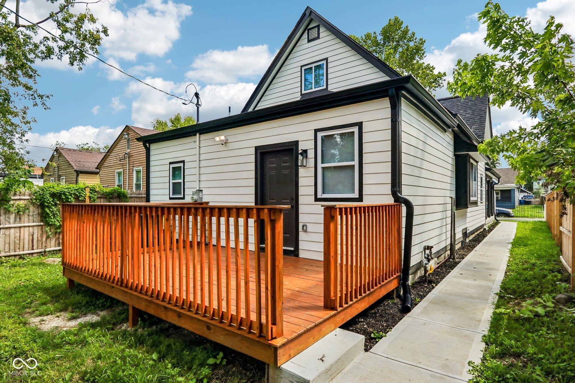 Expansive wood deck with a natural finish, white horizontal siding, black trim, and a concrete side path