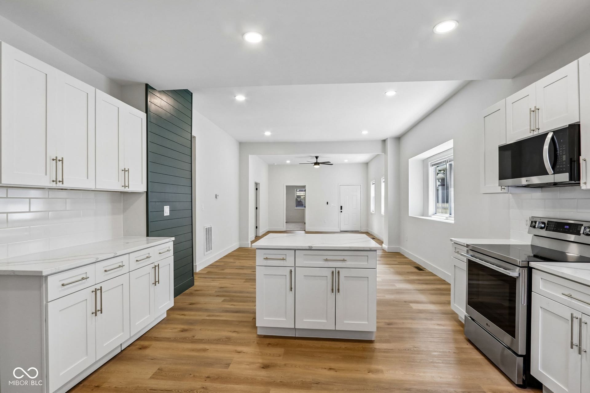 Open-concept kitchen featuring white shaker cabinetry, stainless steel appliances, wood-finish flooring, a central island, and recessed lighting