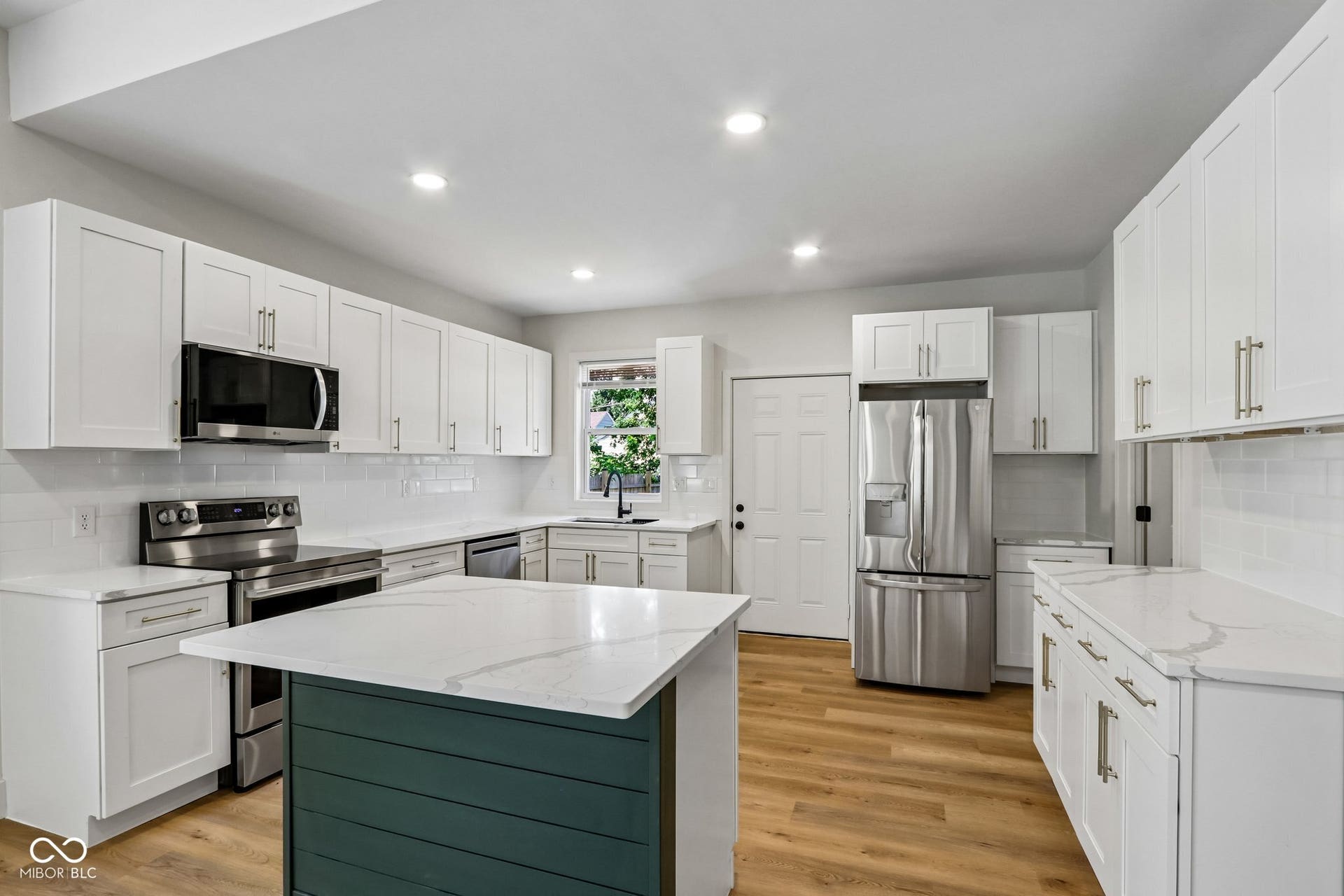 Kitchen featuring white cabinetry, stainless steel appliances, quartz countertops, a shiplap island base, and wood-finish flooring