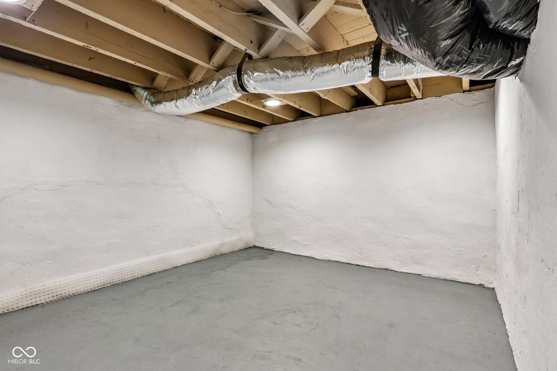 Unfinished concrete floor with white painted walls and visible ceiling joists