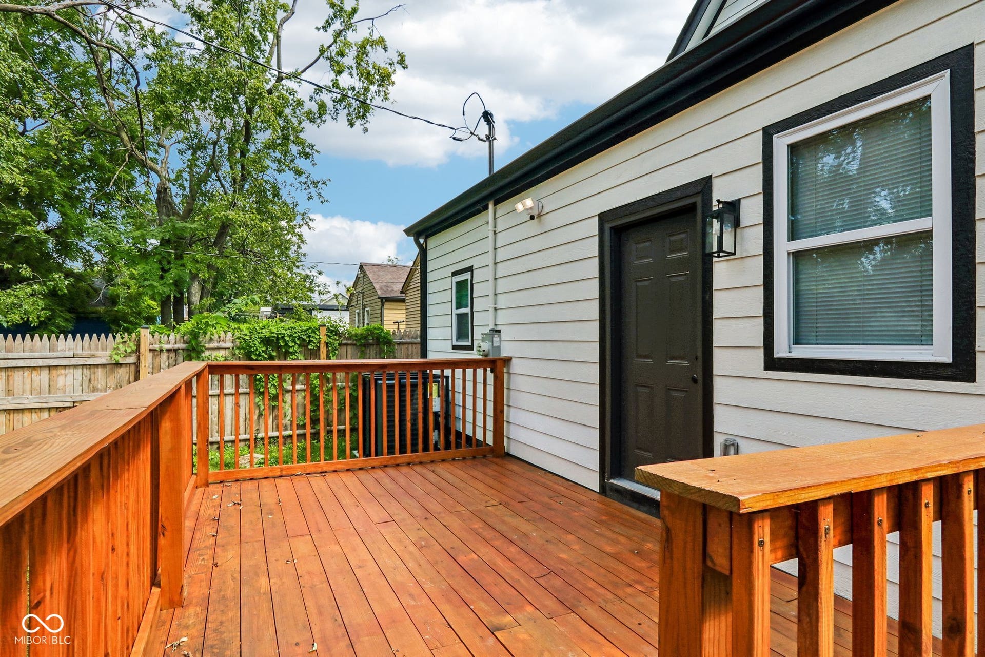 Expansive wood deck with wood railings, white horizontal siding, dark trim, and a paneled exterior door