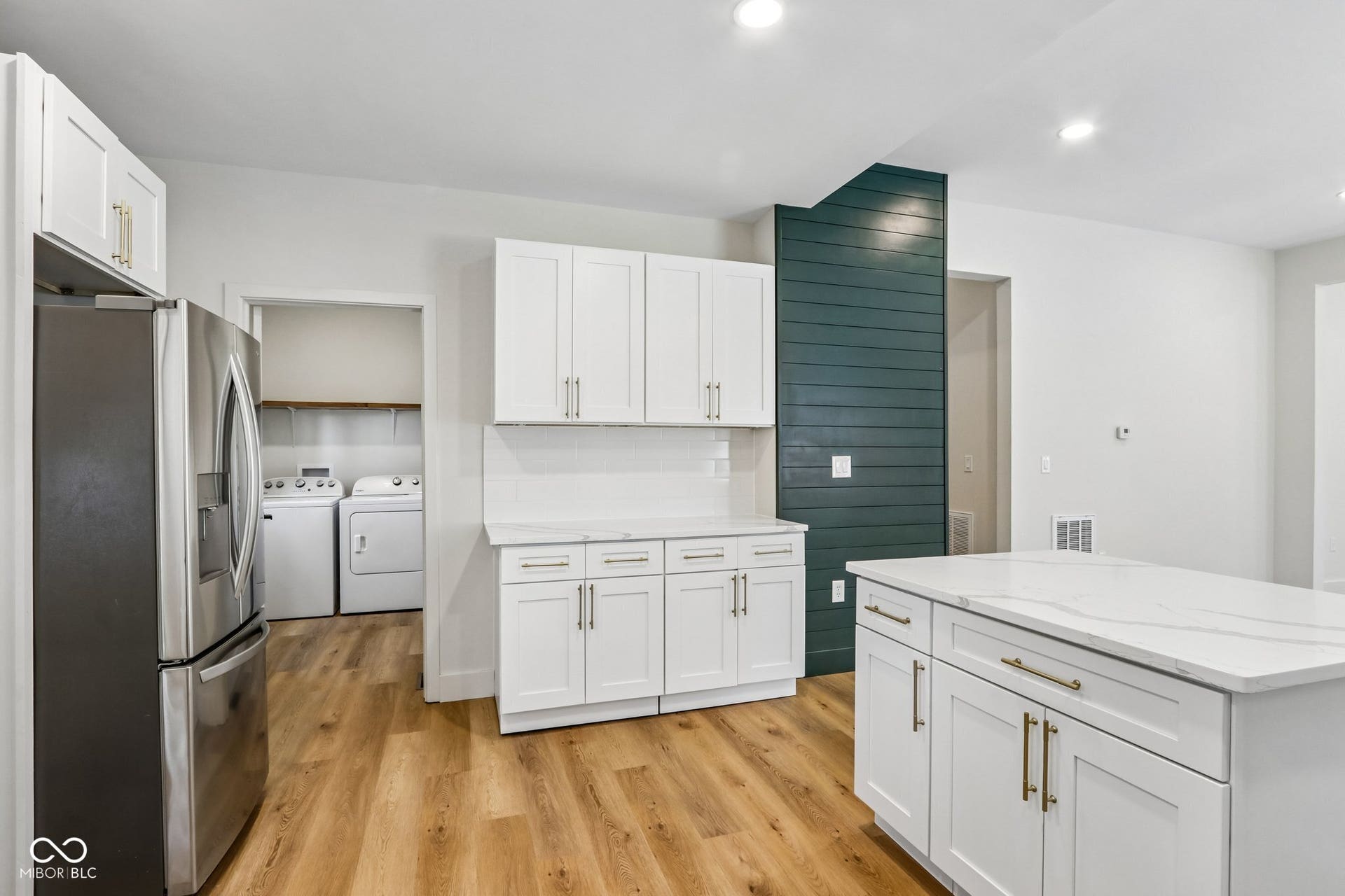 White shaker cabinetry with gold-tone hardware, wood-finish flooring, recessed lighting, and a kitchen island featuring a light-toned countertop