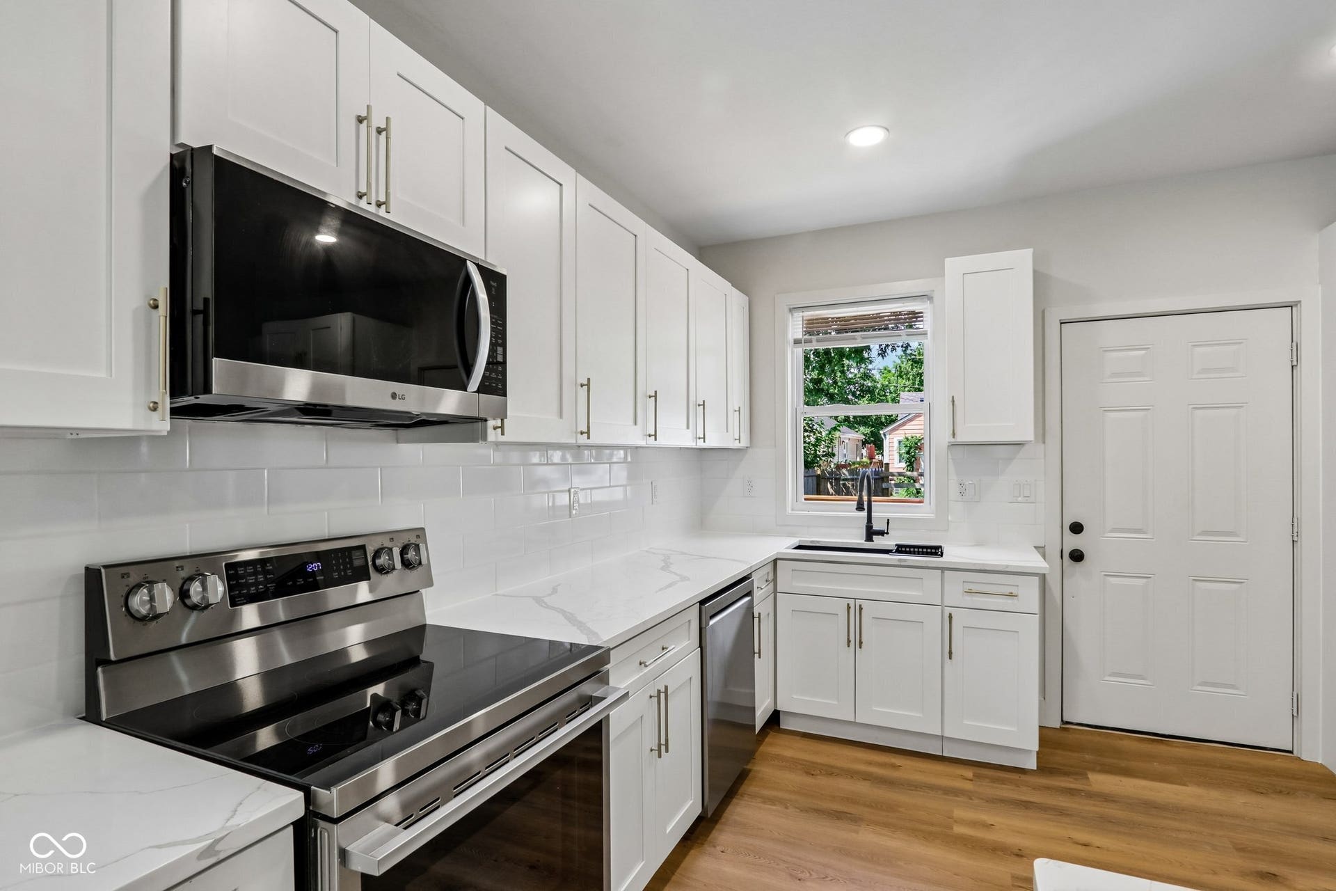 Updated kitchen featuring white shaker cabinetry with stainless steel hardware, subway tile backsplash, black quartz countertops, and stainless steel appliances including a convection range and over-the-range microwave