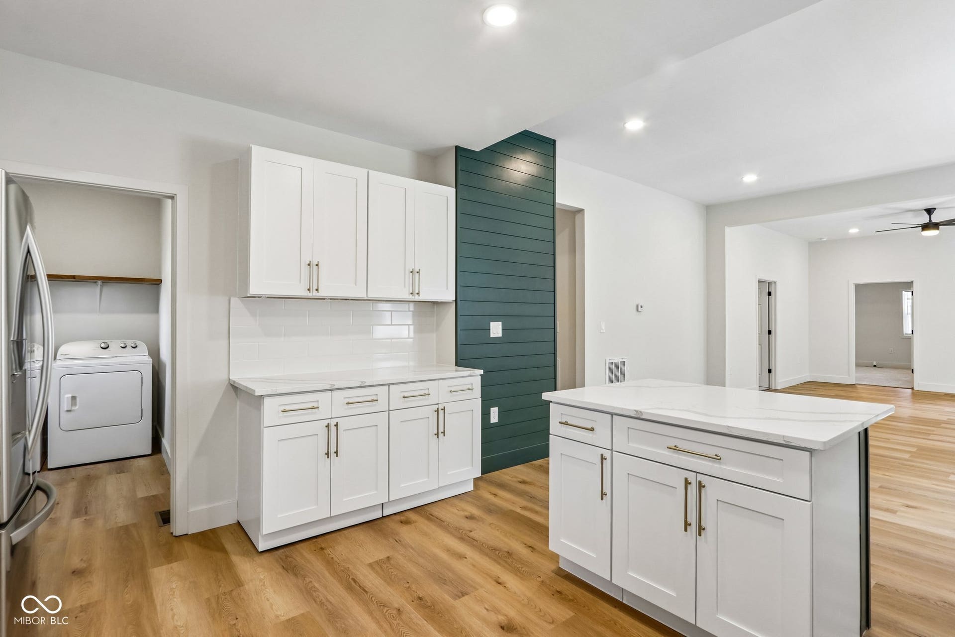 White shaker cabinetry, light-colored countertops, wood-finish flooring, recessed lighting, and a dark teal accent wall
