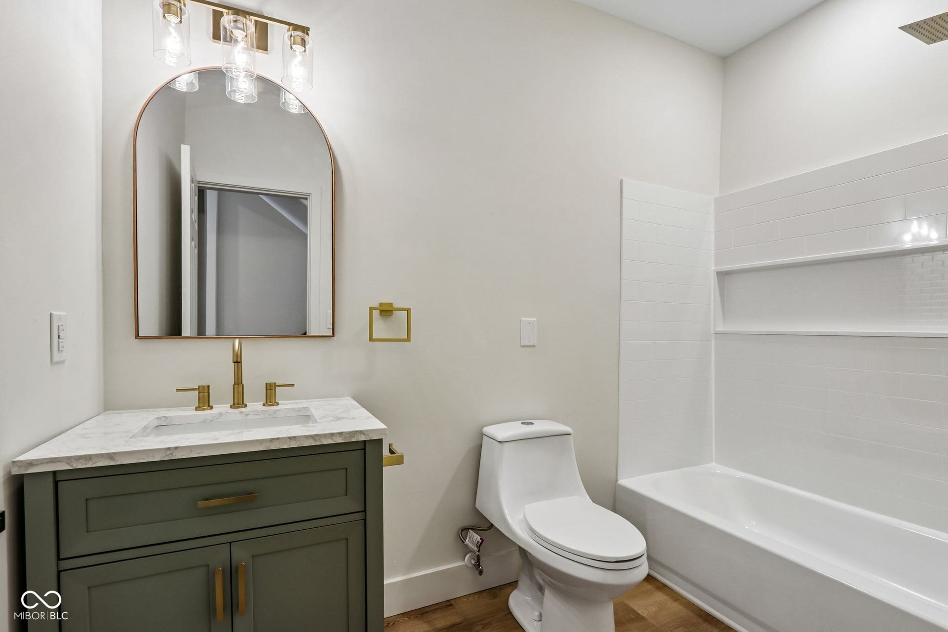 Modern vanity with a white countertop and brass-finish fixtures, complemented by a white subway tile shower surround and a built-in bathtub