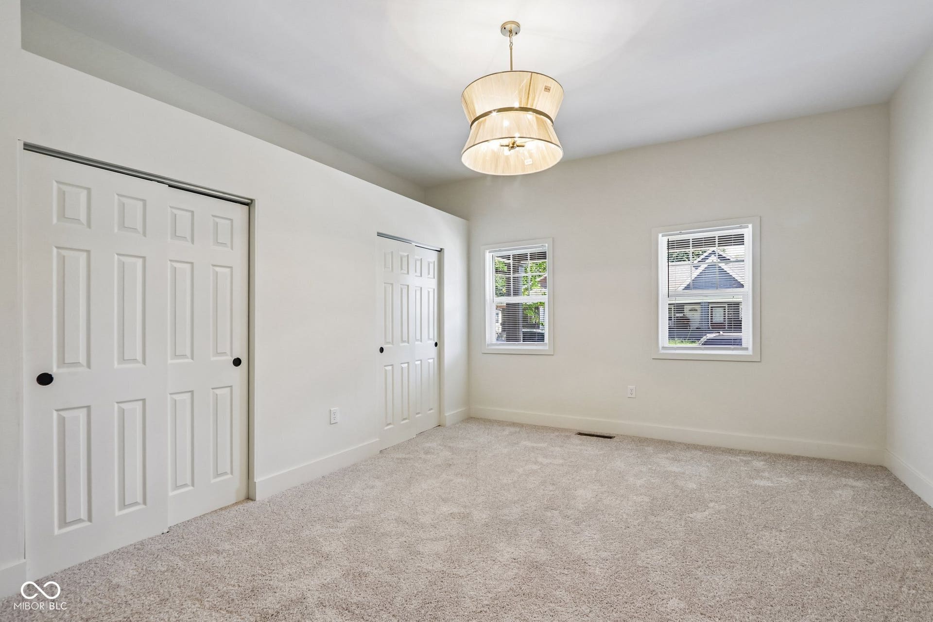 Vaulted ceiling, two built-in closet systems, two windows, textured carpeting, and a drum pendant light fixture