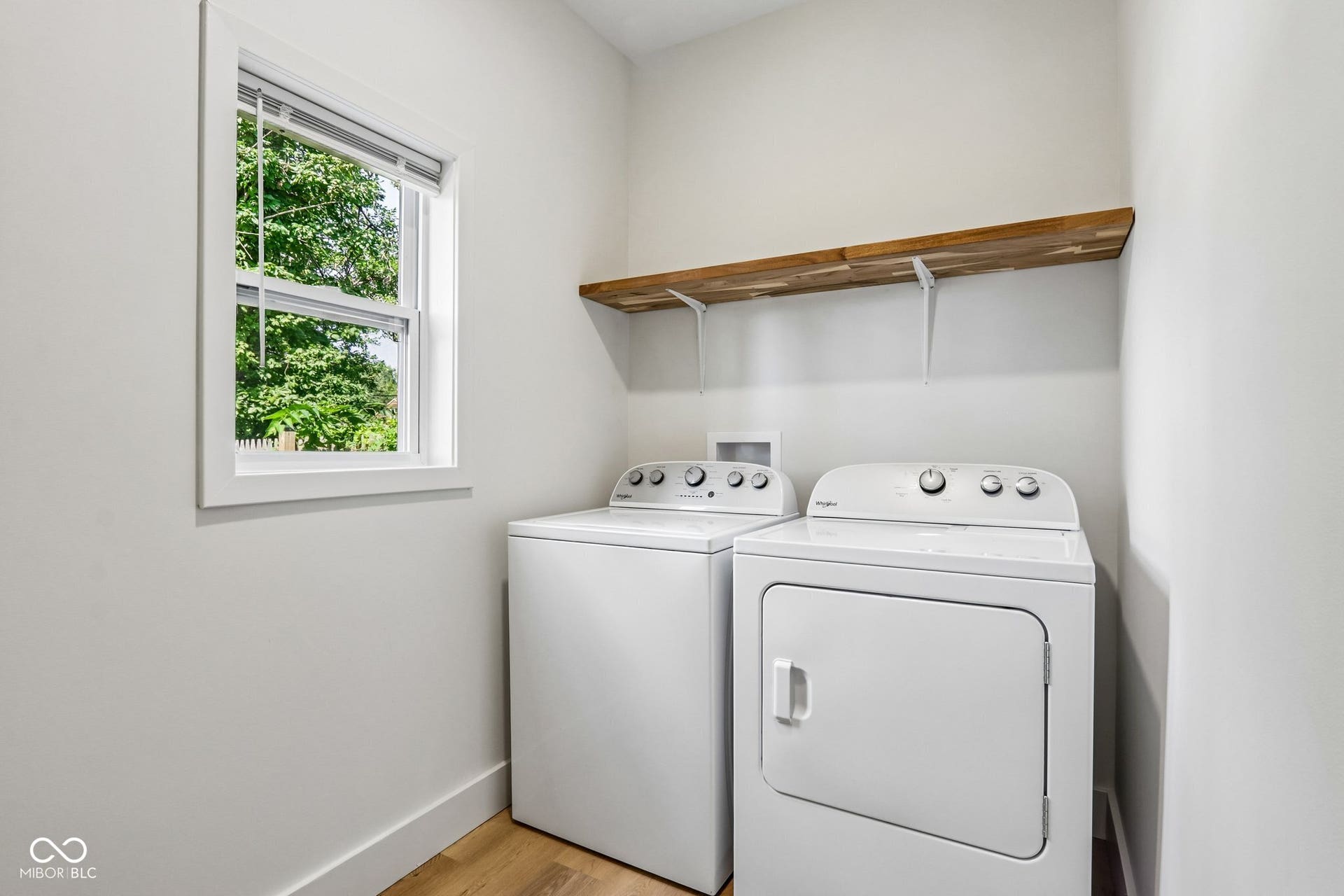 Dedicated laundry area featuring a window, wood-finish shelving, and wood-finish flooring