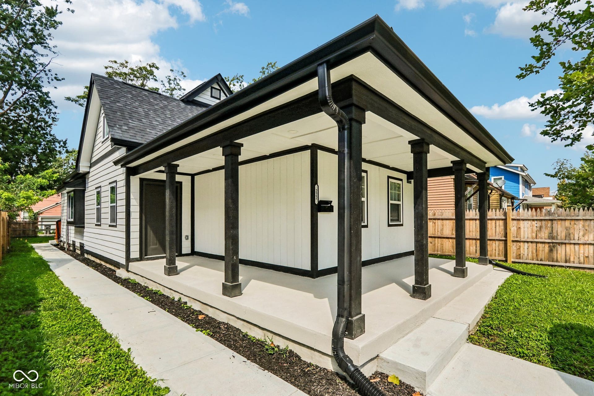 Gable roofline with black shingles, white siding with black trim, concrete front porch with black support columns, white soffit, and black gutters