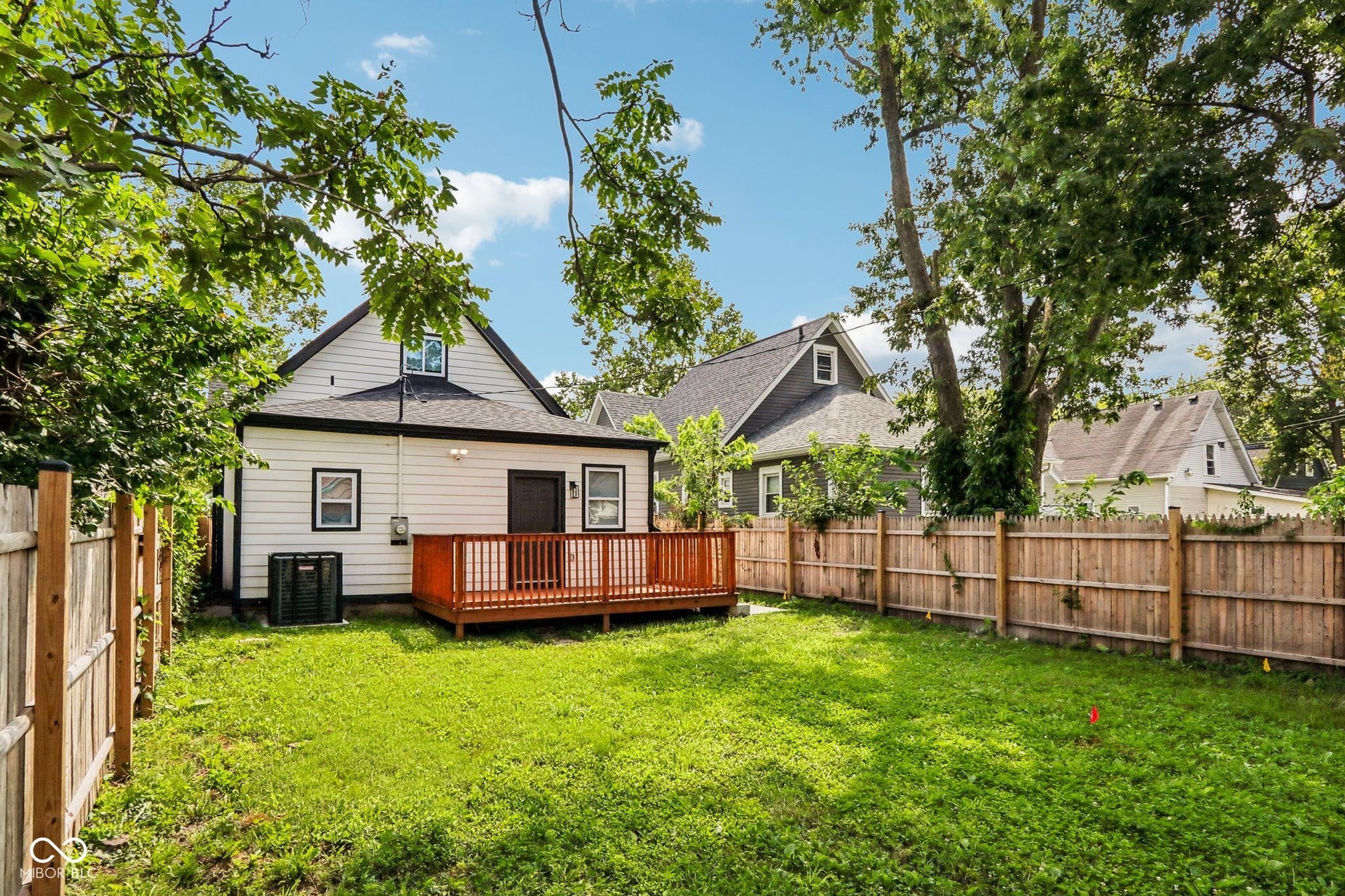 Expansive backyard featuring a wood privacy fence, a manicured lawn, a wooden deck, and a white siding exterior
