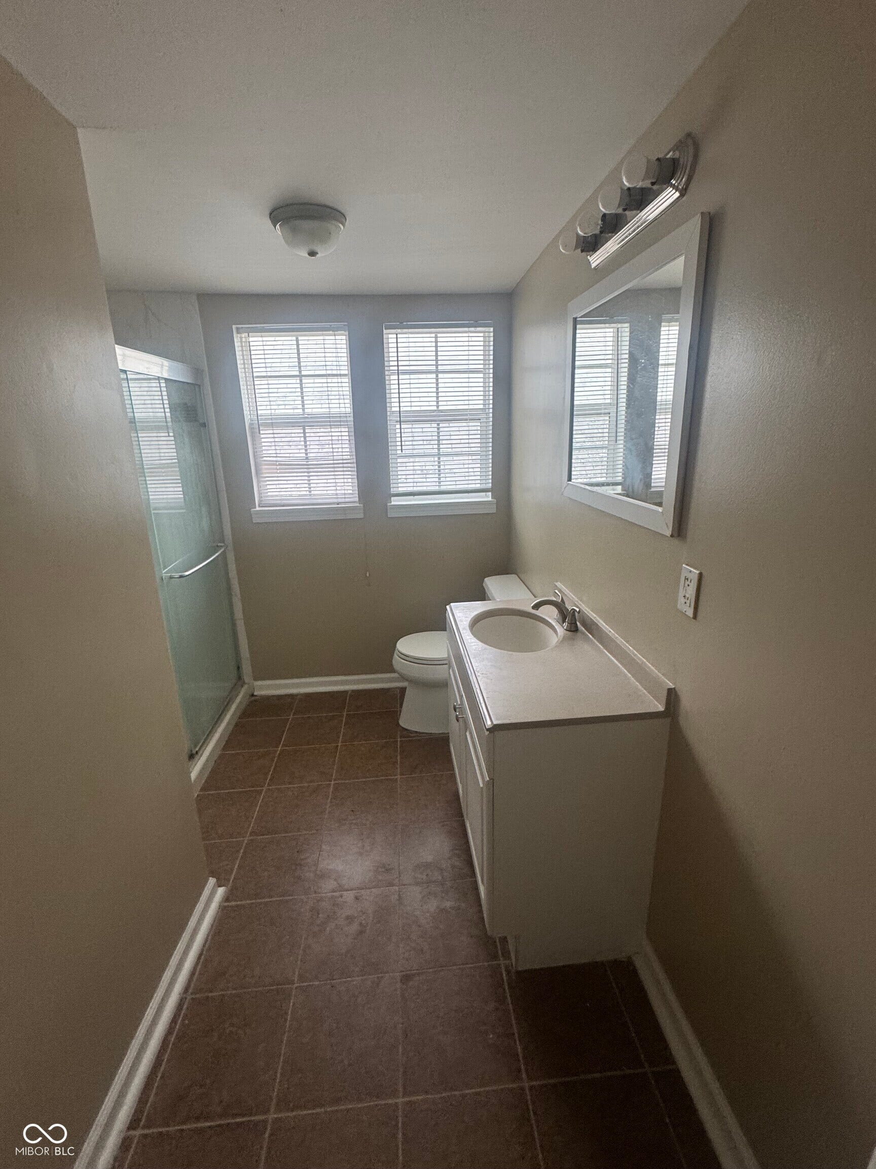 Virtually Altered - Bathroom featuring a white vanity with integrated sink, a framed mirror, a shower enclosure with a clear glass door, and tiled flooring